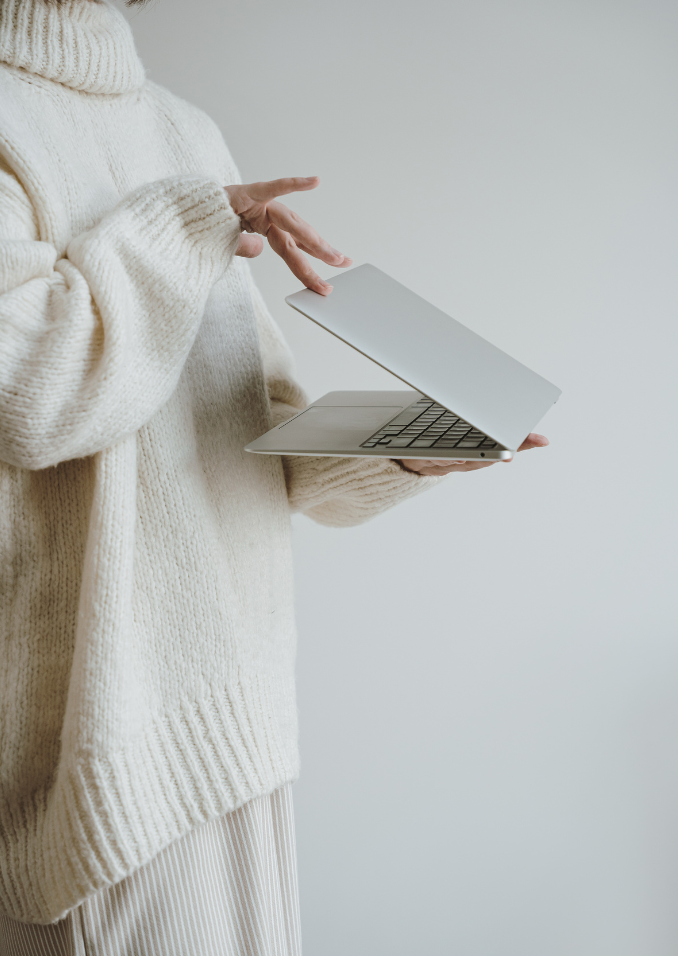 Person in einem weißen Pullover hält einen Laptop in der Hand und benutzt ihn.