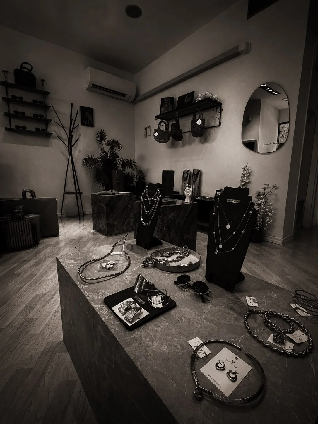 Interno di un negozio di gioielli con vari orecchini, collane e braccialetti esposti su un tavolo e manichini. Decorazioni e scaffali con oggetti decorativi e specchio rotondo sulla parete.