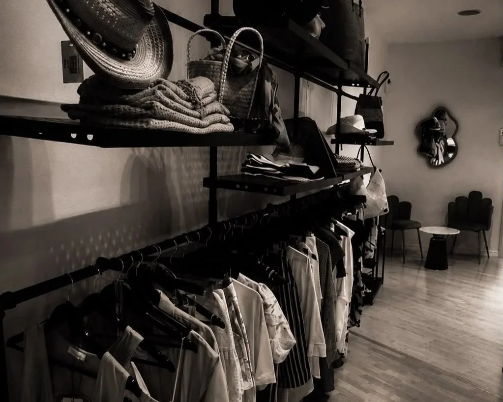 Scaffale con cappelli, borse, vestiti e accessori in un negozio o showroom, con sedie e tavolino sullo sfondo.