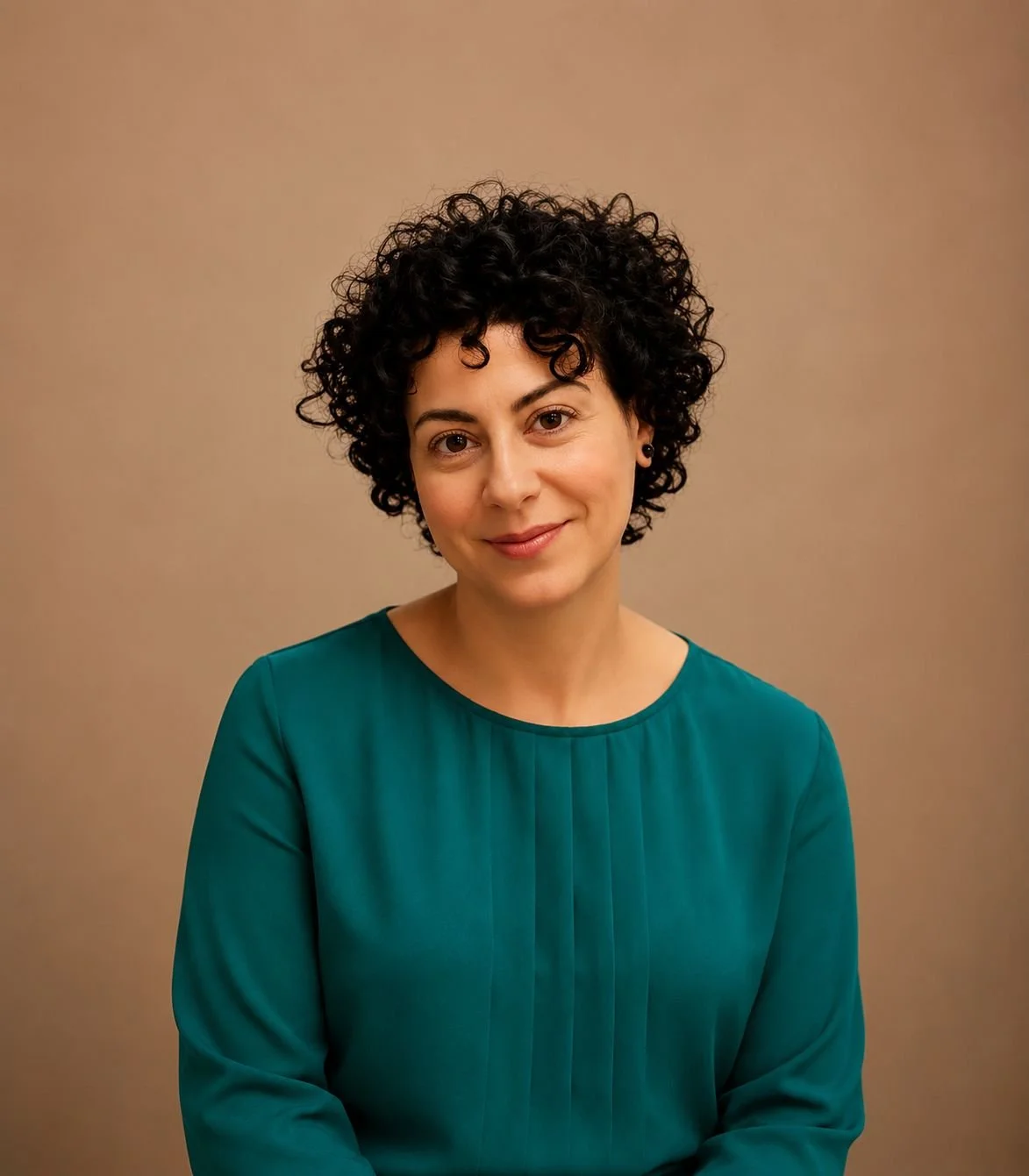 Portrait of a woman with short, curly black hair and light skin, wearing a teal blouse, smiling softly against a plain beige background.