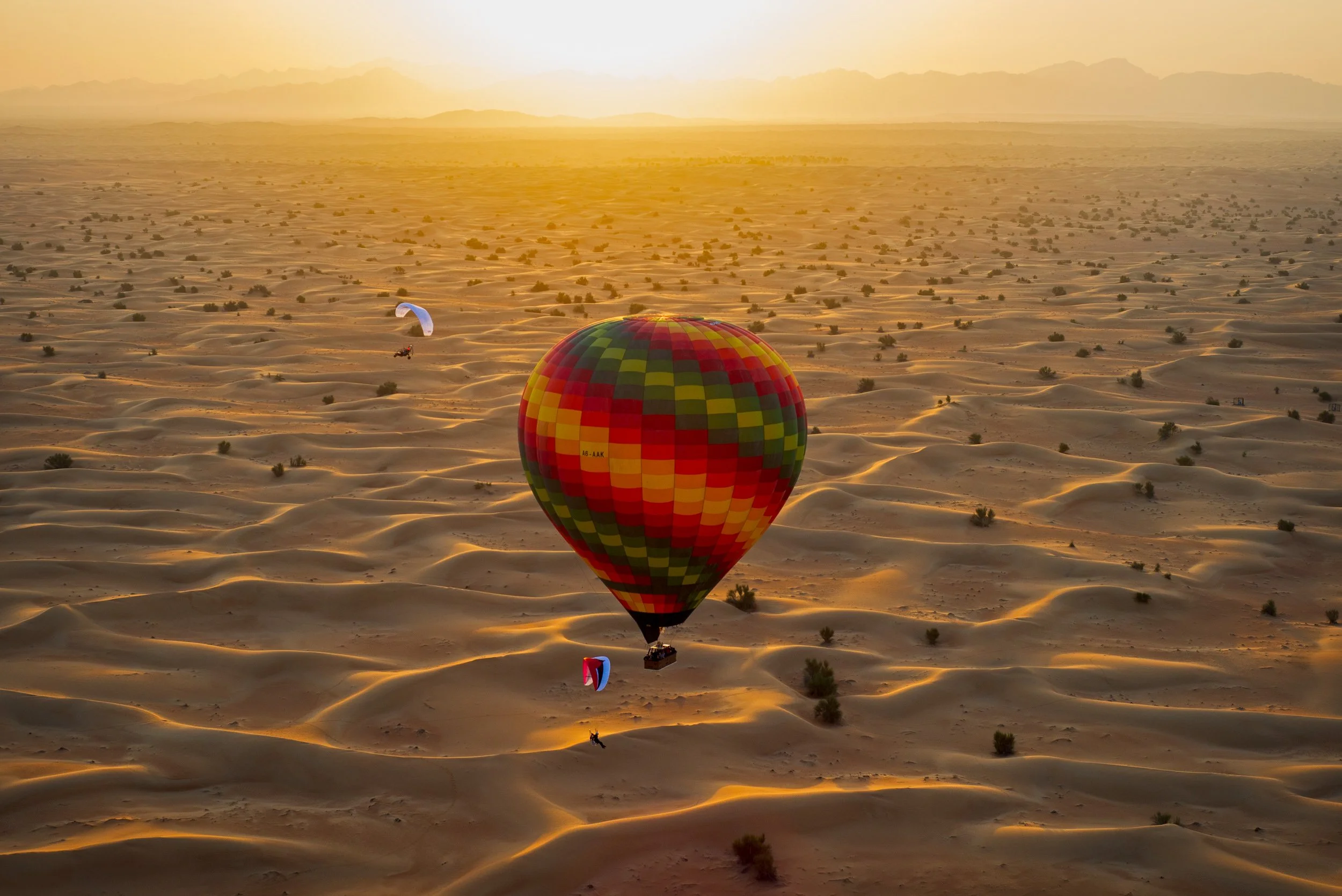 Hot air balloons flying over a desert landscape at sunset.
