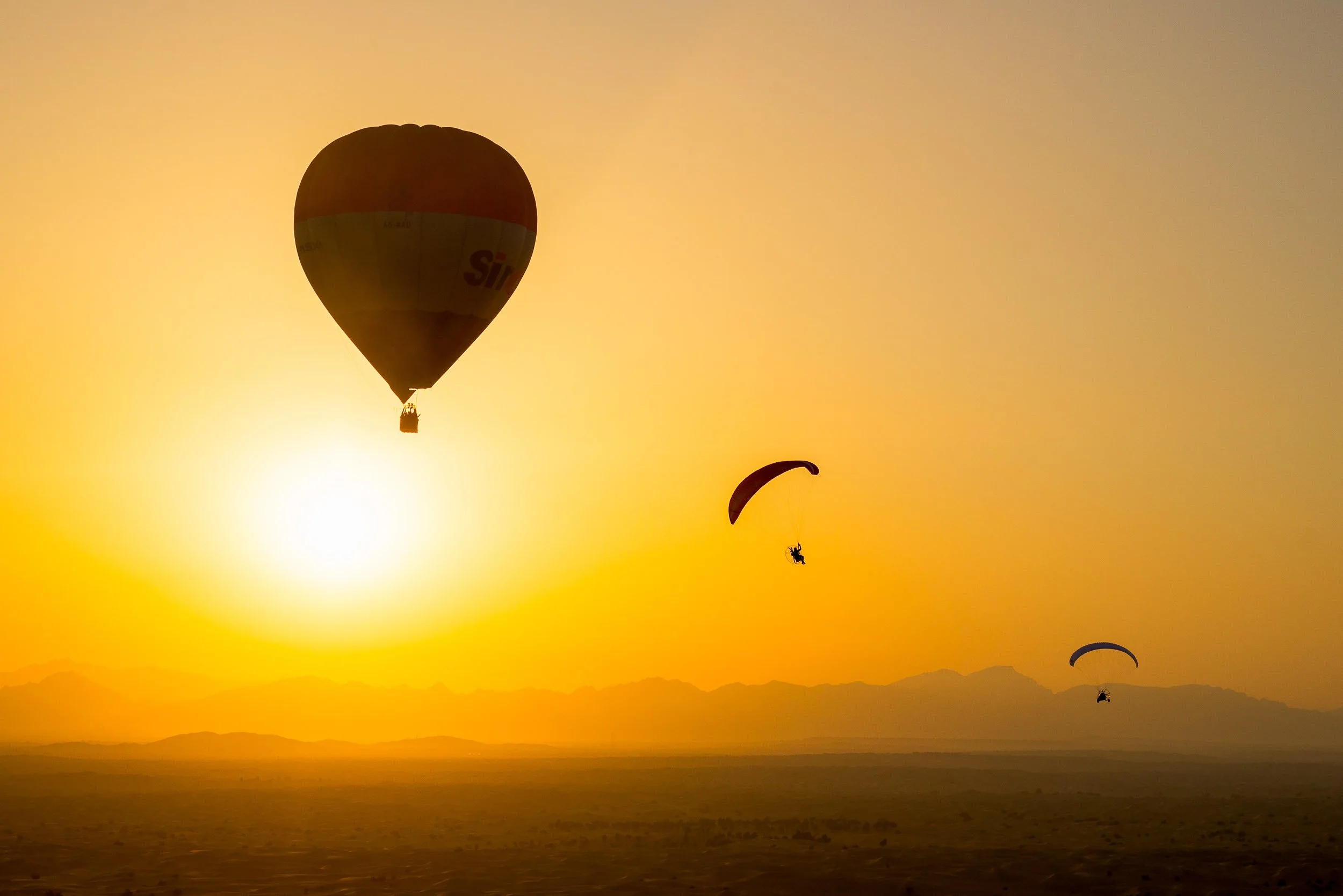 Hot air balloons floating in the sky during sunset, with mountains and a landscape below.