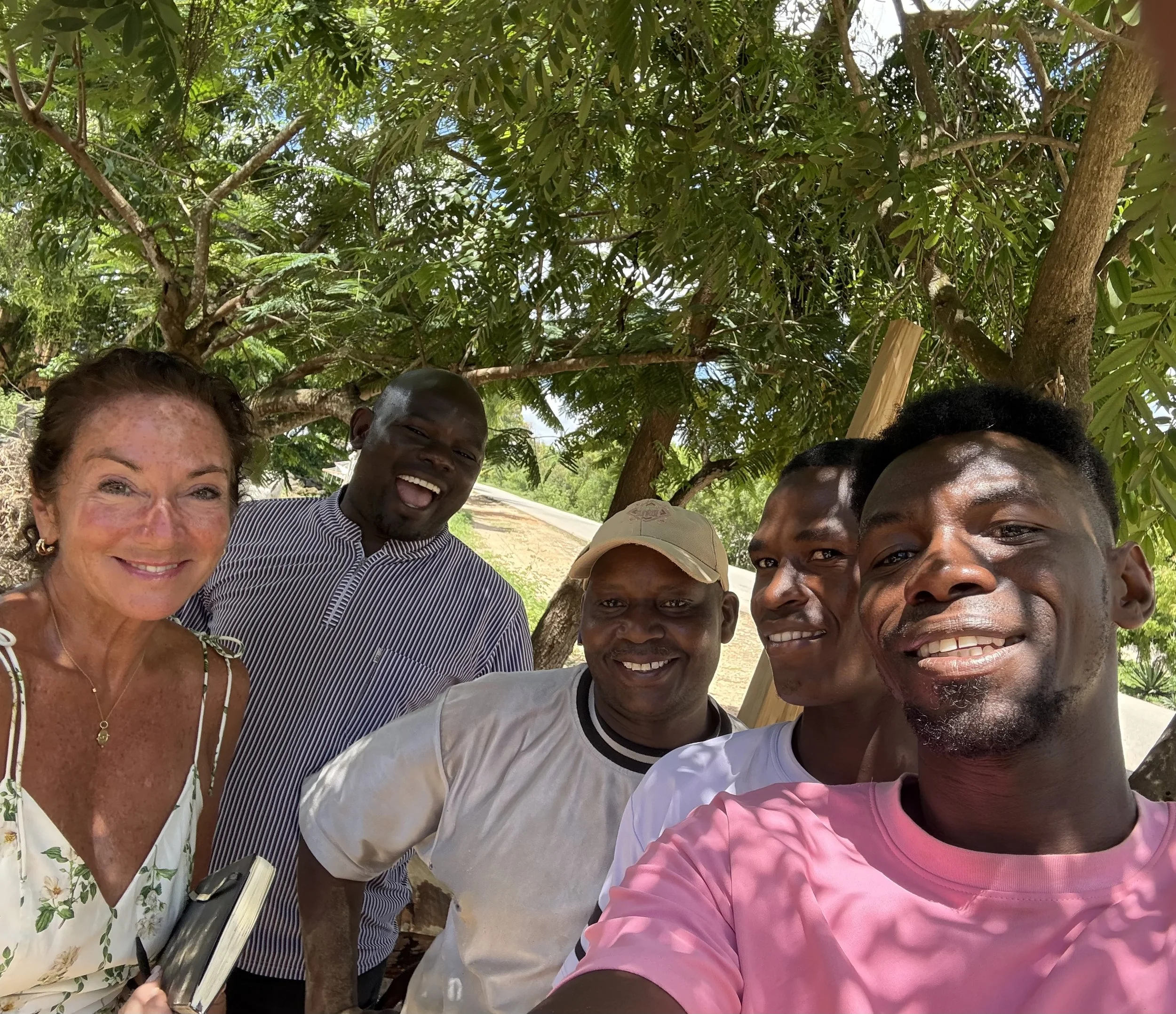 A group of people taking a selfie outdoors with a large tree and green foliage in the background.