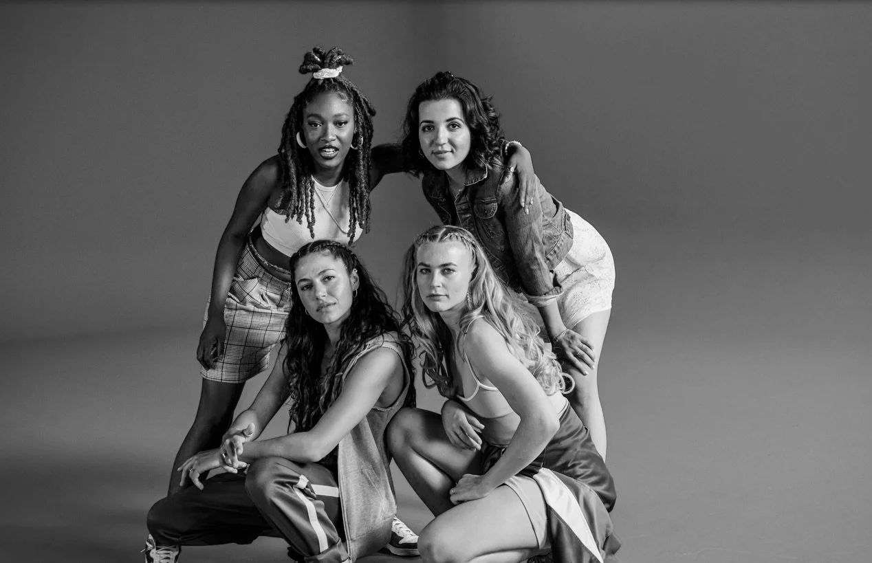 Black and white photo of five diverse young women posing together against a plain backdrop.