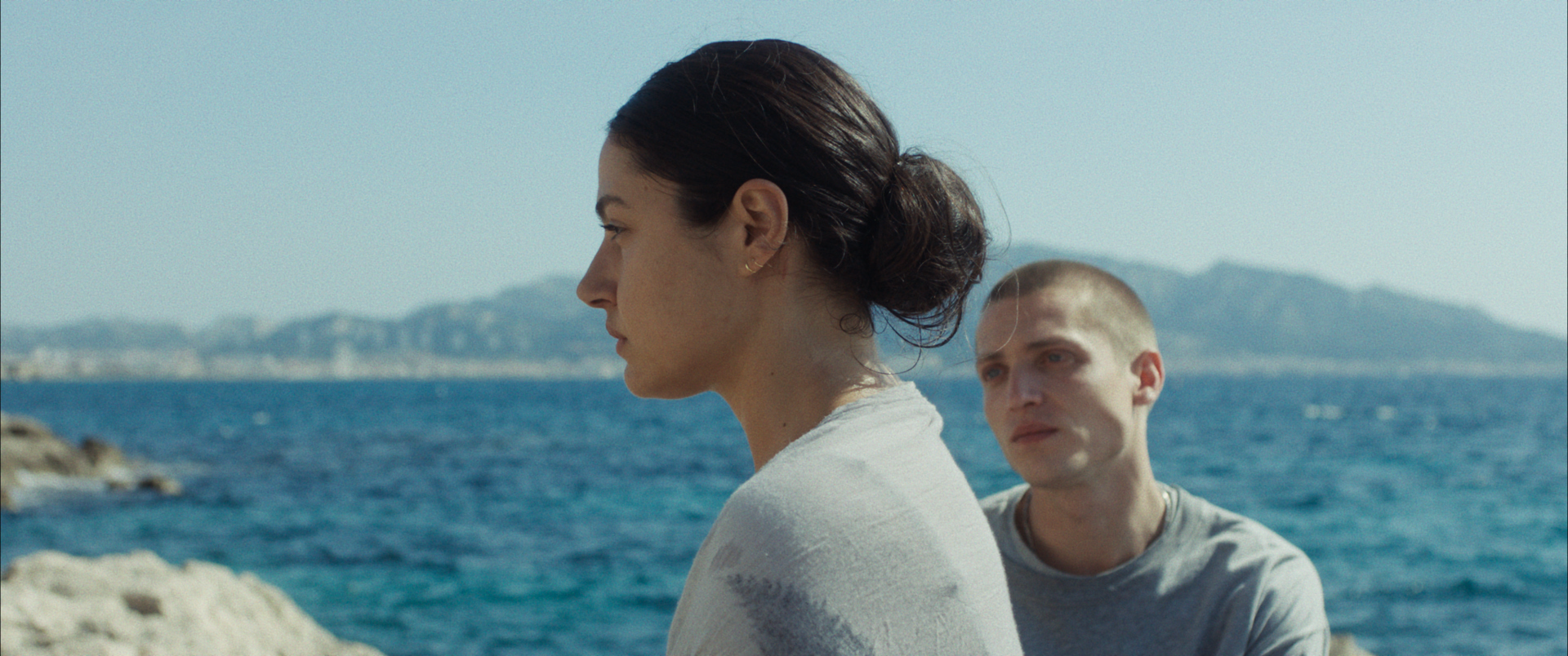 Woman starring out on to the sea, man looking at her from behind.
