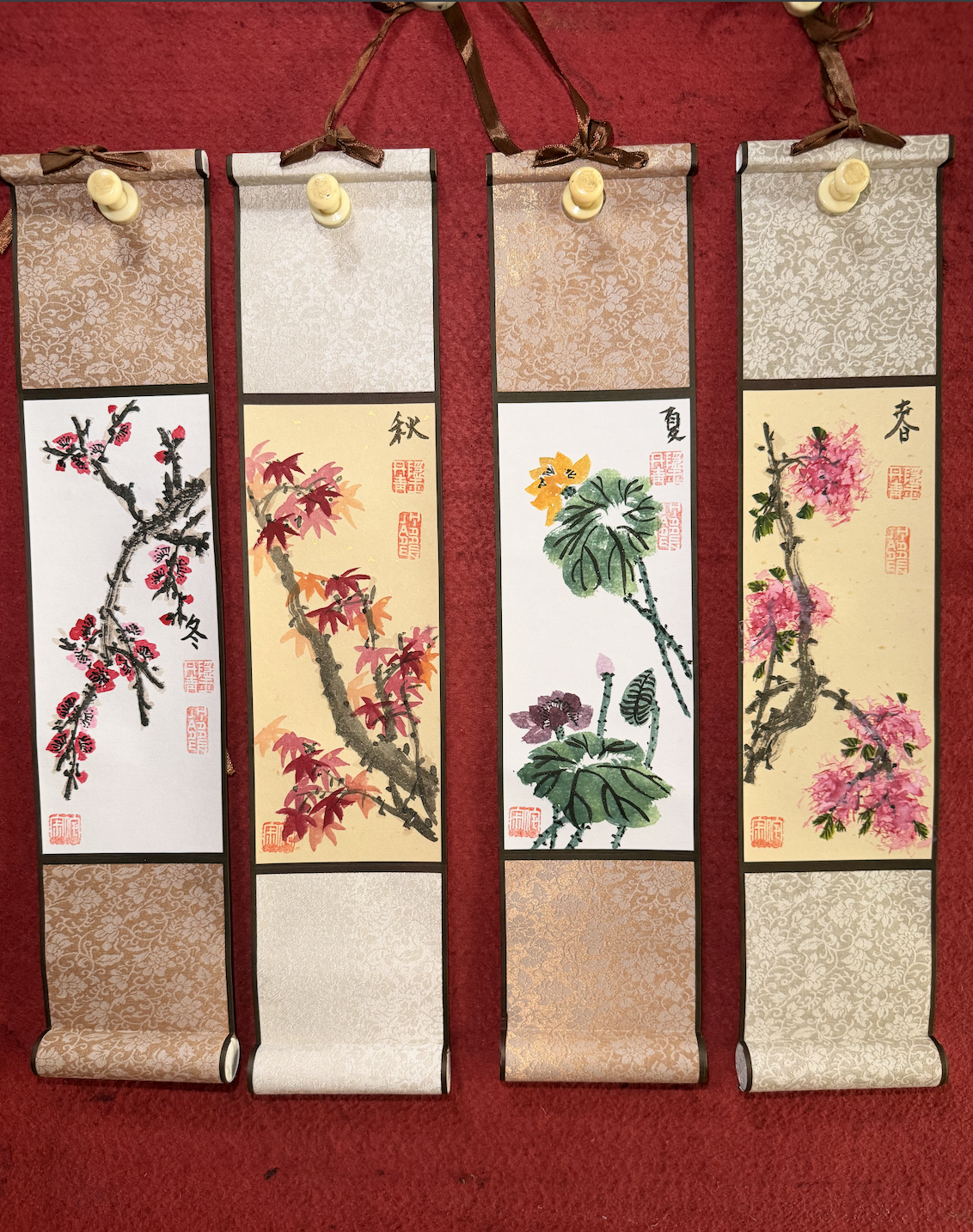 Four traditional hanging scrolls featuring East Asian brush paintings of seasonal flowers and birds.