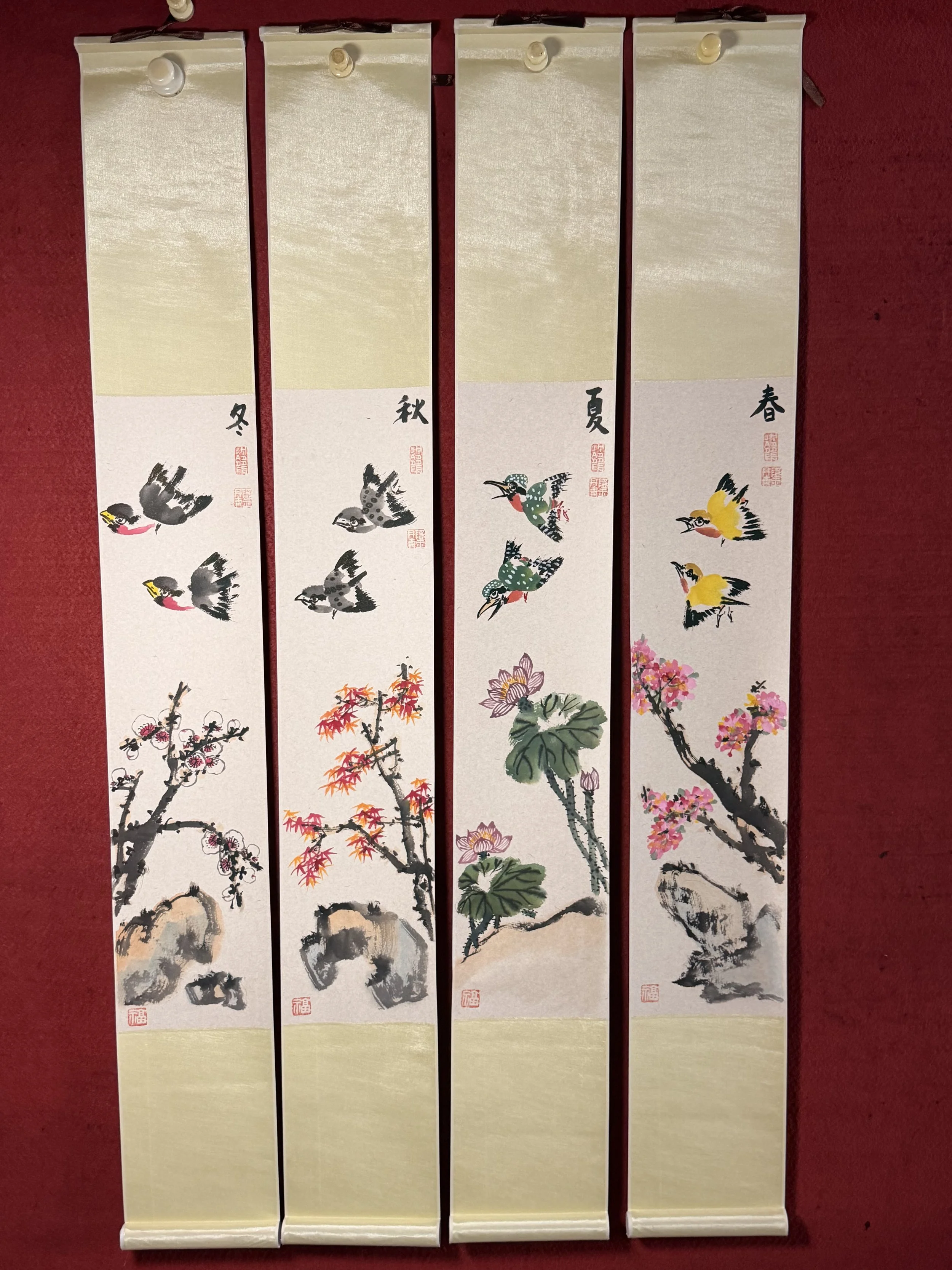 Four vertical Japanese hanging scrolls featuring traditional ink and watercolor paintings of blooming cherry blossom branches and colorful bird illustrations, each marked with red seals and Japanese characters.