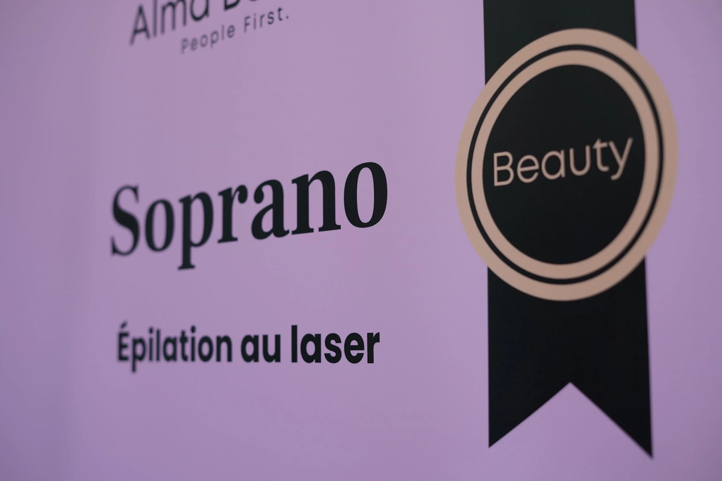 Zoom sur un emballage ou un panneau volant avec le mot 'Soprano' en gros caractères, mentionnant l'épilation au laser, avec un symbole ou logo indiquant 'Beauty'.
