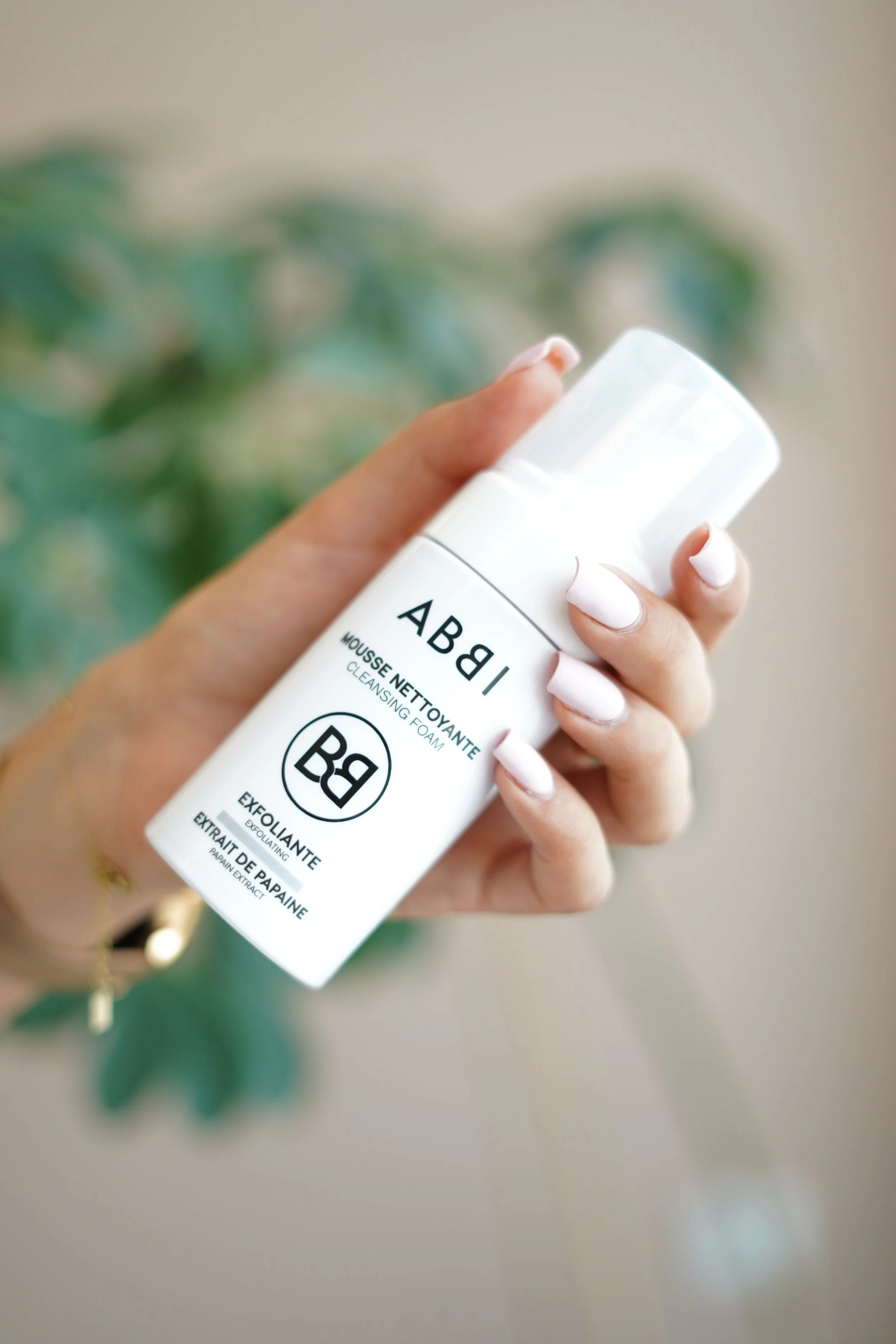 Manucure avec ongles blancs, tenant un tube de mousse nettoyante pour peau à base d'extrait de papaye.