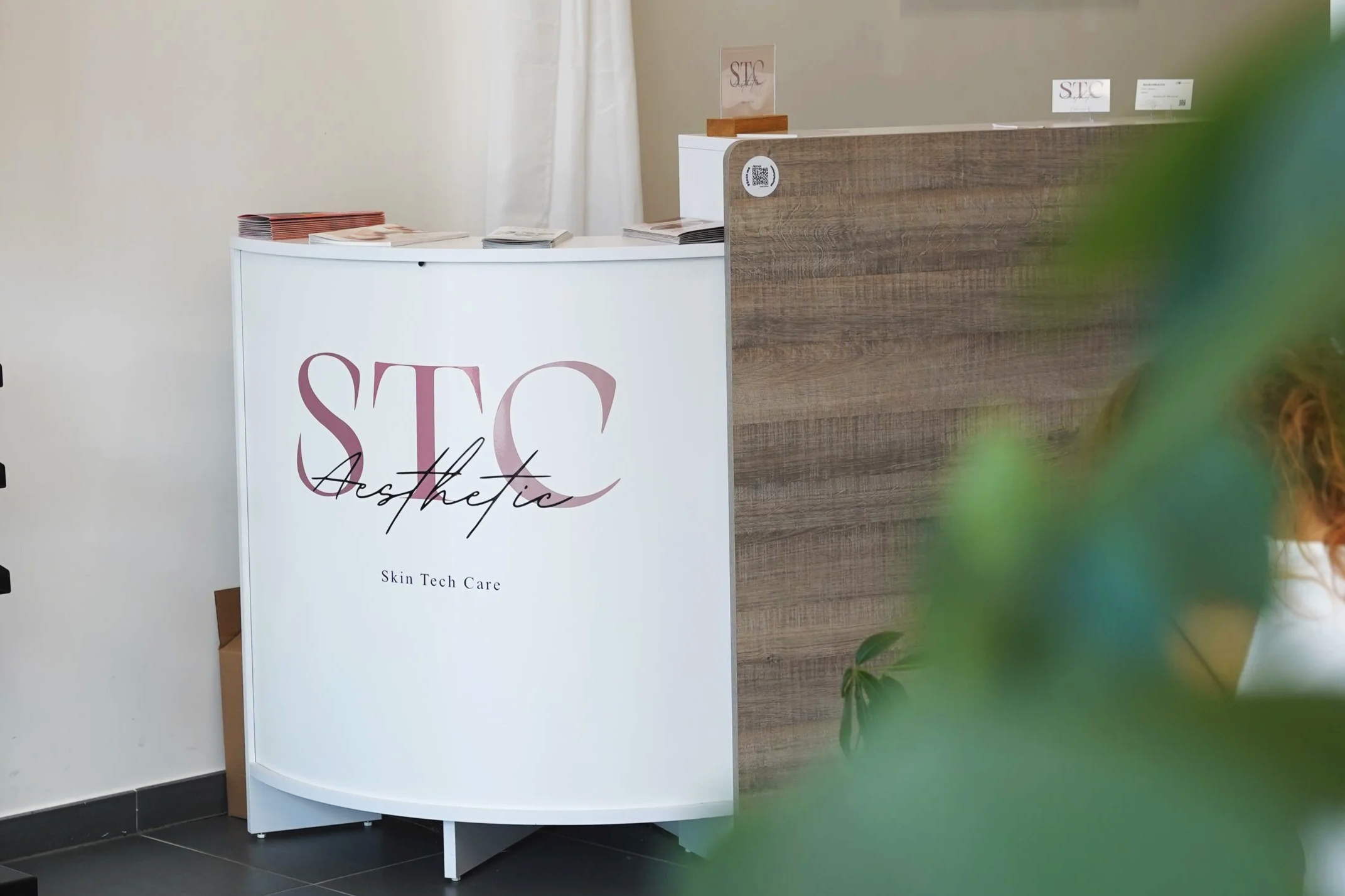 Un comptoir en bois et blanc avec des brochures et une affiche indiquant 'S.T.C' pour une marque de soins de la peau, dans un intérieur moderne.