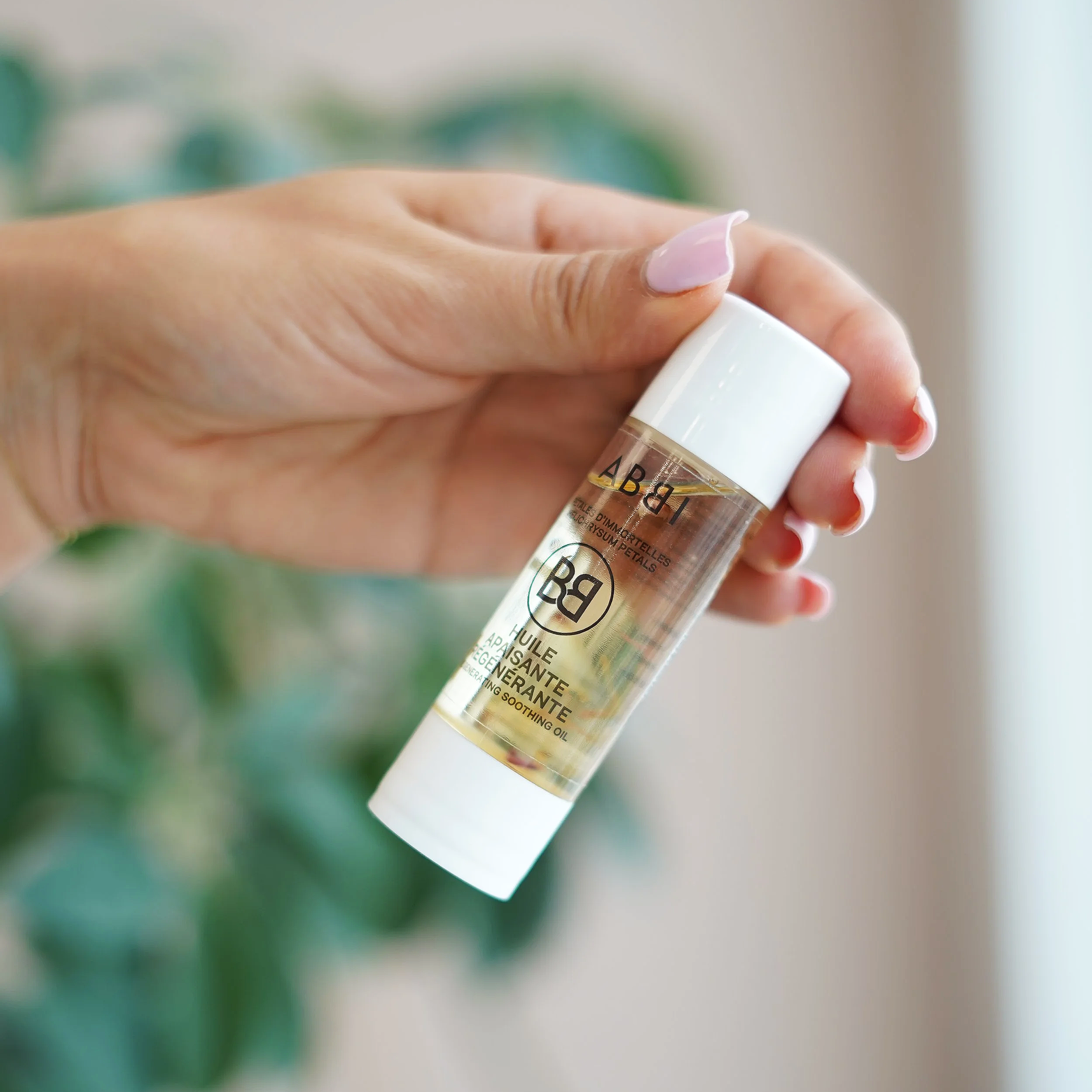 Mains tenant une petite bouteille de gel hydroalcoolique, sur un fond flou.