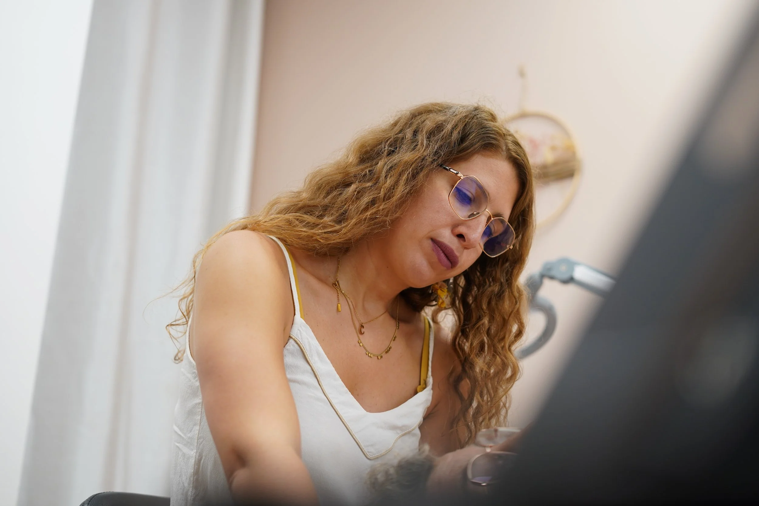 Jeune femme avec lunettes de soleil, portant un débardeur blanc, assise à un bureau, utilisant un ordinateur portable.