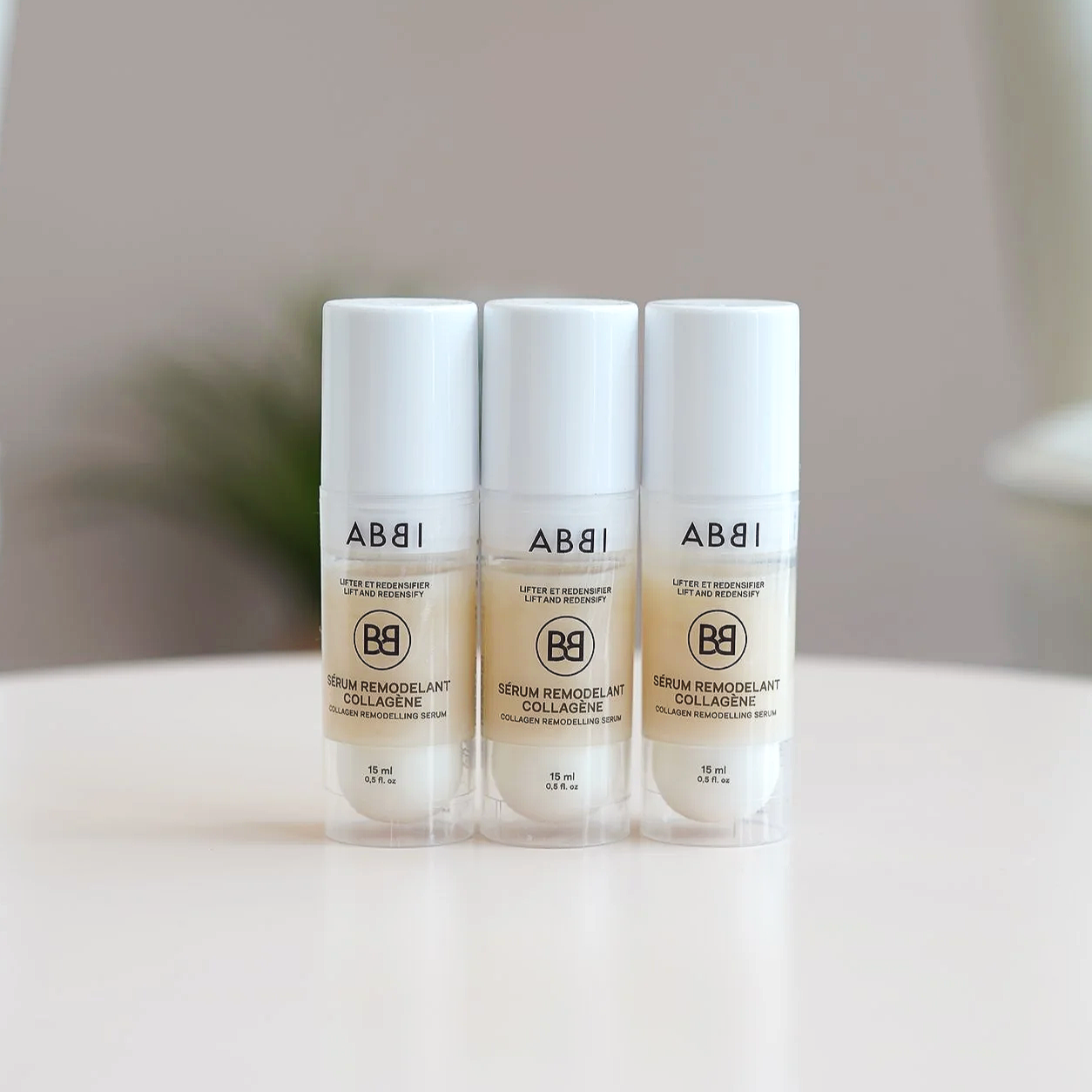Trois tubes de sérum remodelant au collagène alignés sur une surface blanche, avec fond neutre et flou.