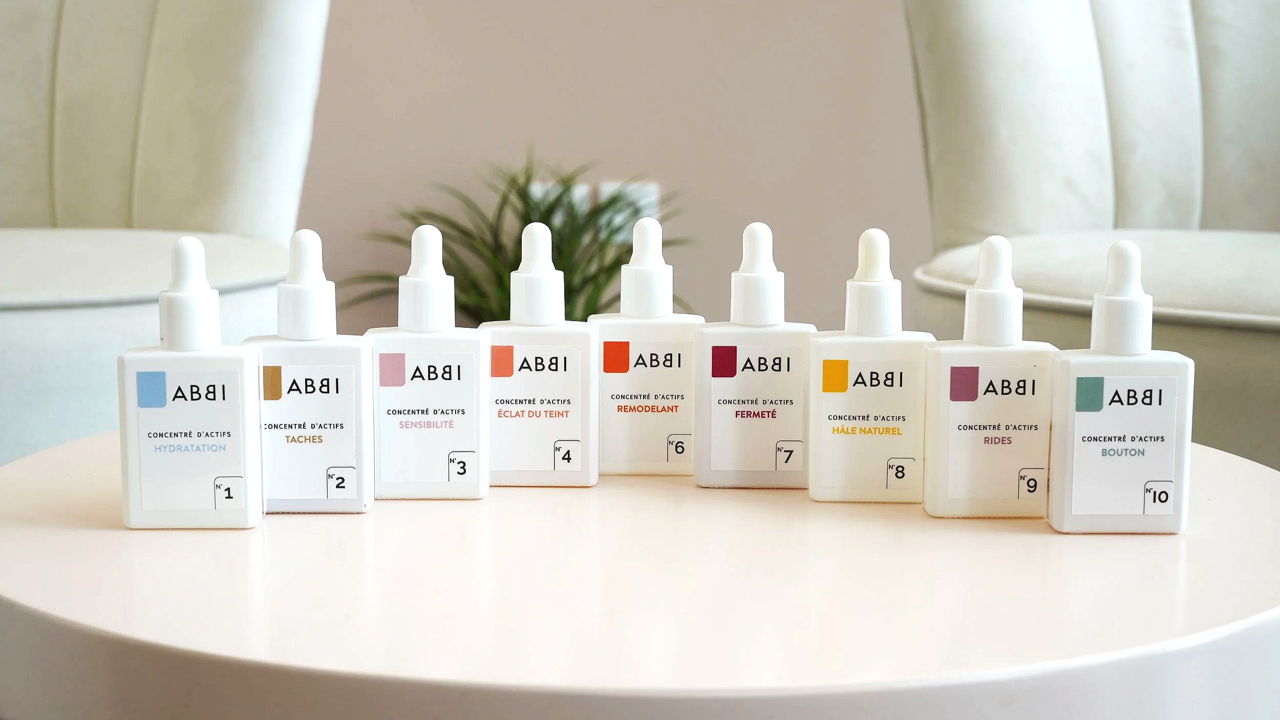 Une collection de flacons de soins de la peau alignés, chacun avec une étiquette indiquant leur fonction, comme hydratation, taches, sensibilité, éclat du teint, remodelant, fermeté, hâle naturel, rides, bouton.