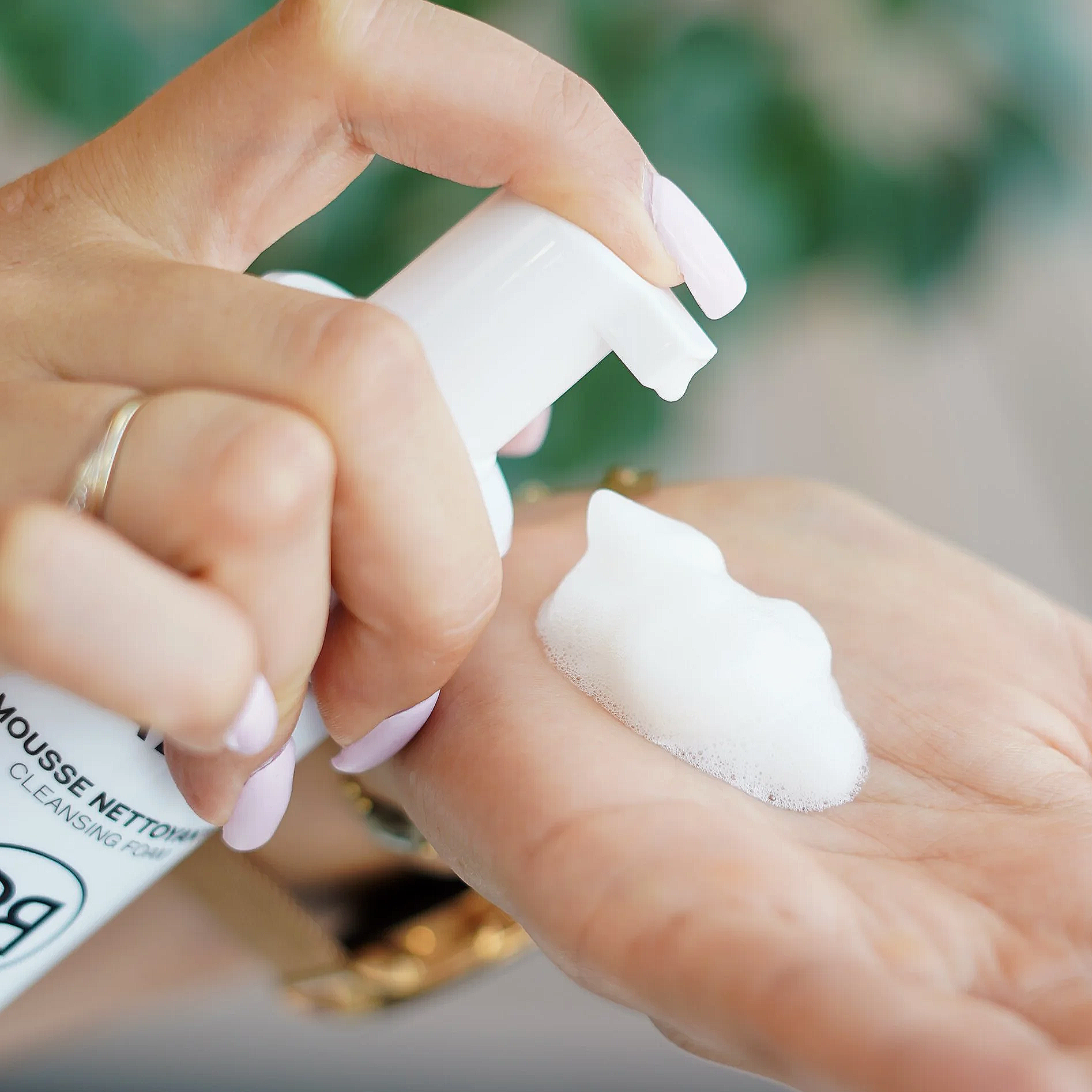 Main tenant un flacon de nettoyant pour laver le visage. La main applique le produit sur la peau du visage.