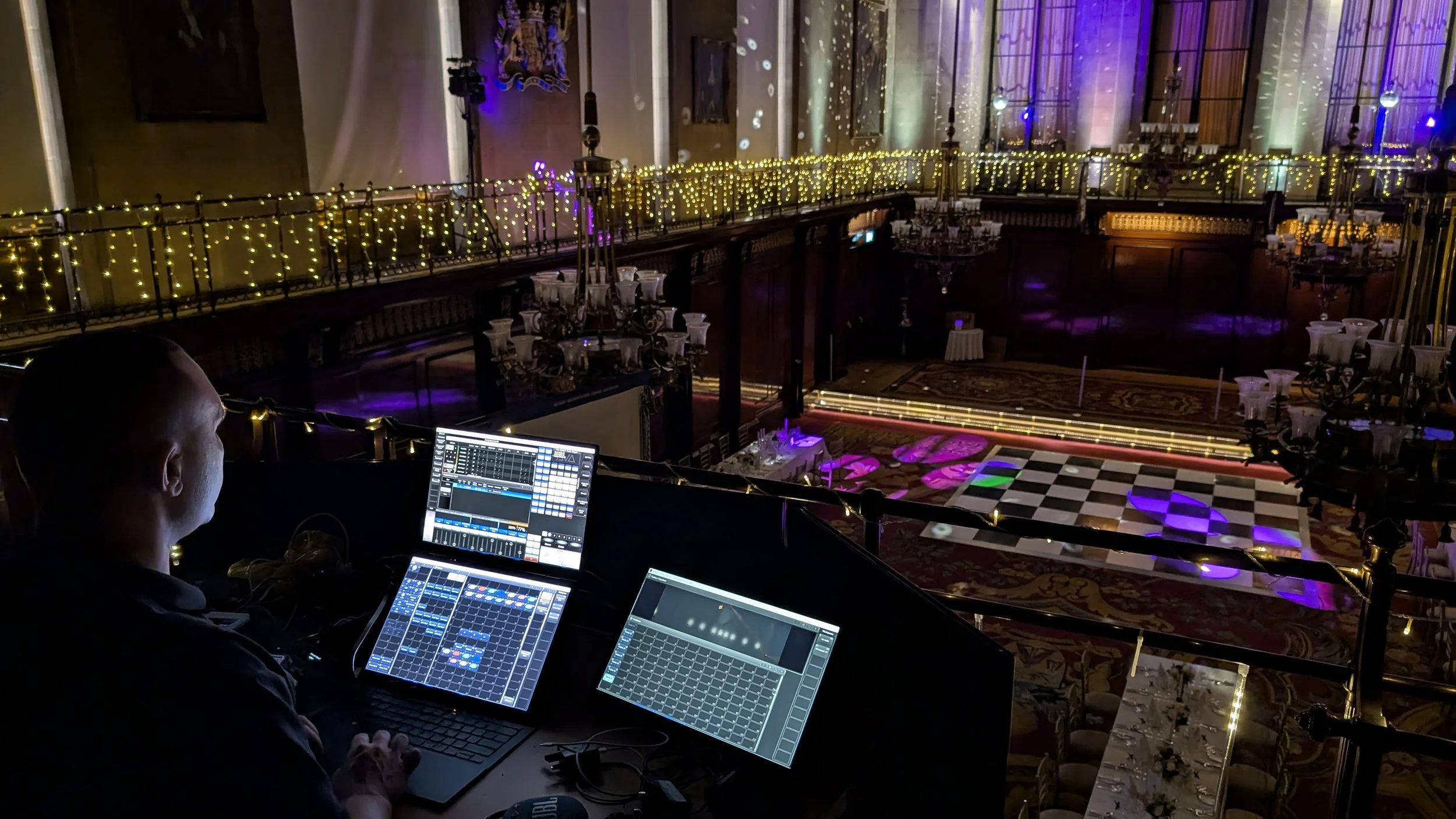 A sound engineer is operating digital music equipment in a decorated ballroom with mood lighting for a wedding party