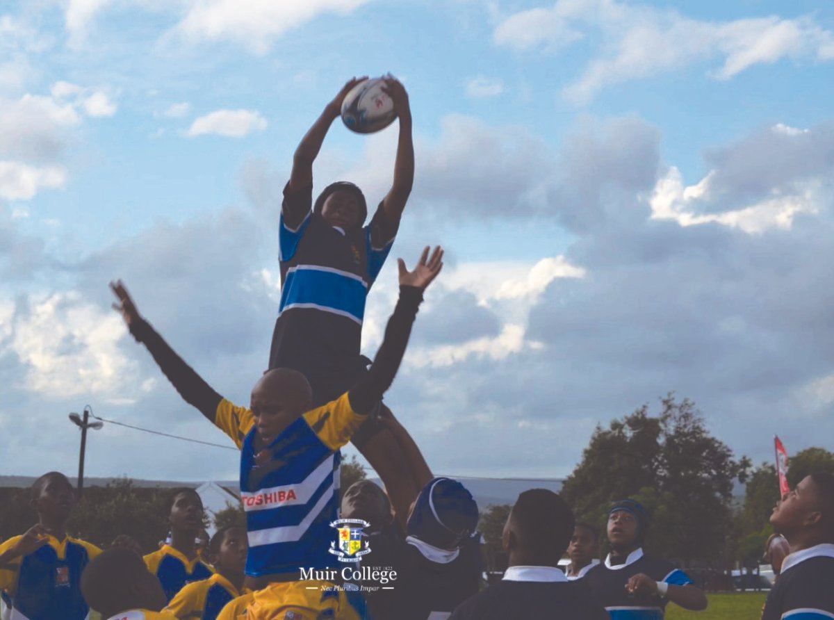 A rugby match with players jumping to catch the ball in the air during daytime, with a clear sky and some clouds, at Muir College.