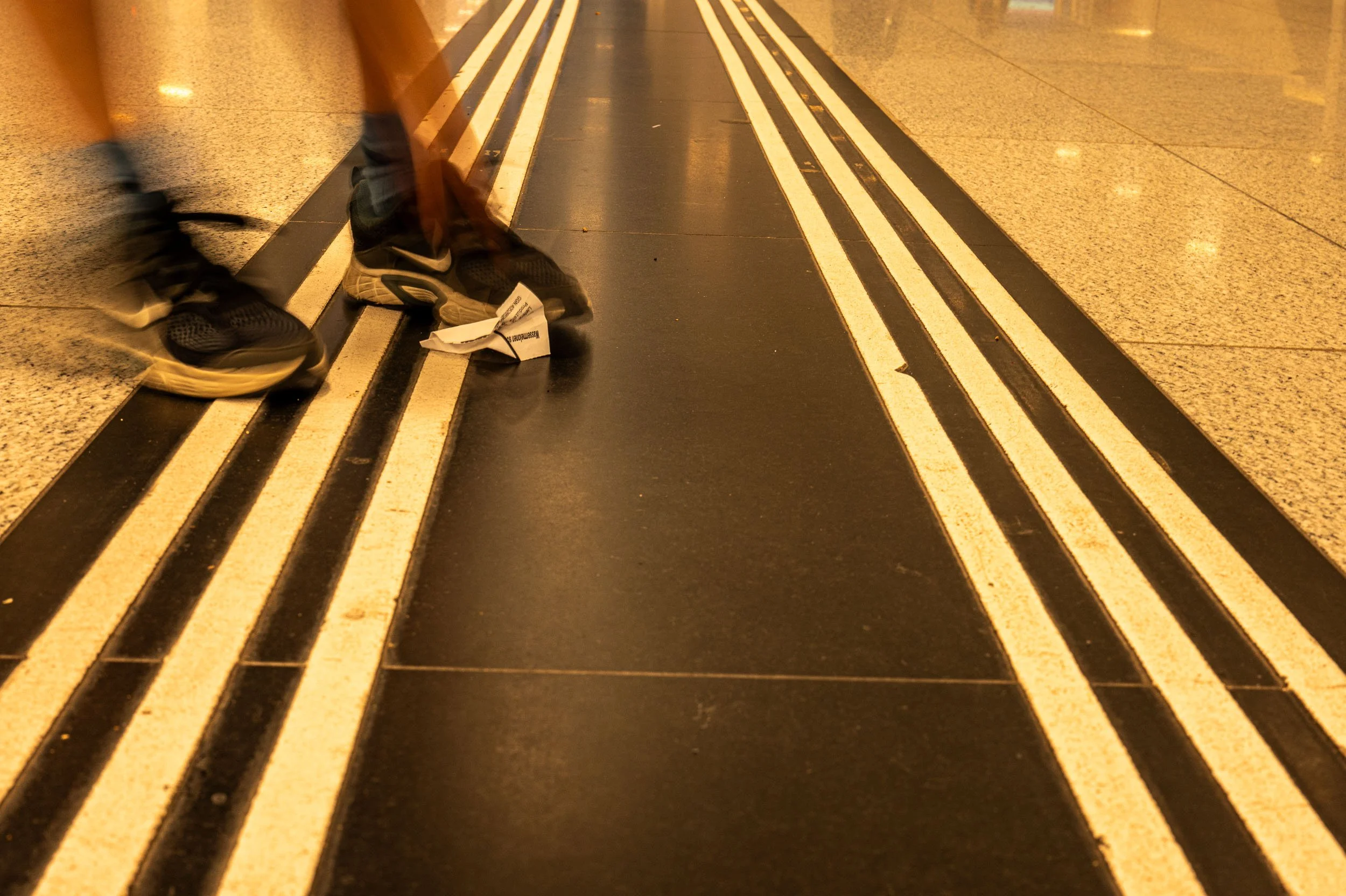 Close-up of the feet of two people walking in a corridor with black and white striped floor markings.