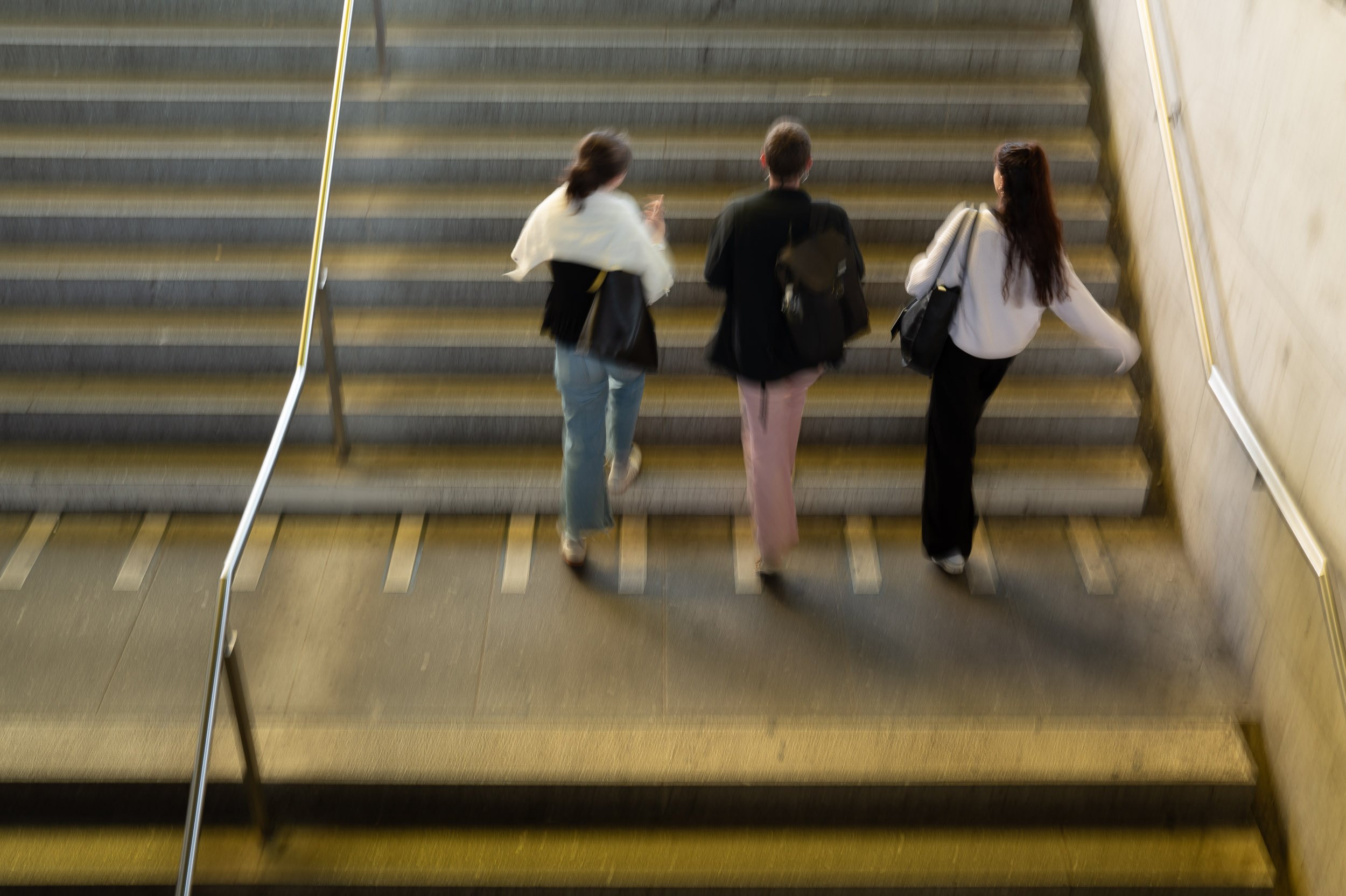 Three women walking up a staircase with a gold-colored handrail.