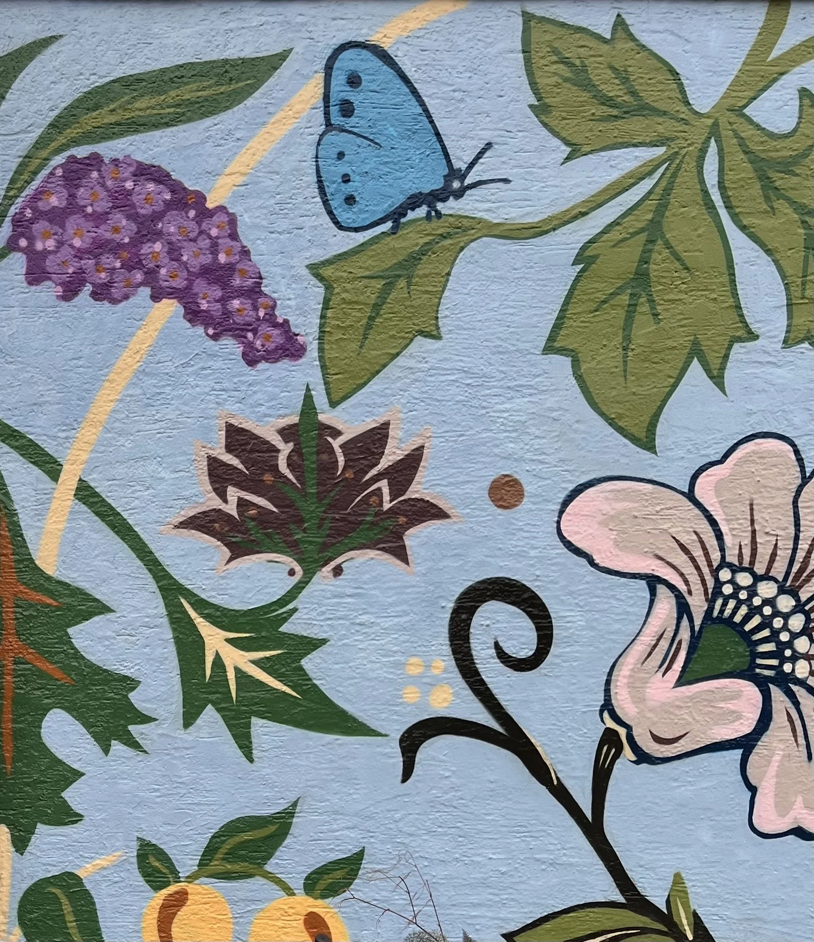 A wall mural showing leaves, plants and butterflies painted on a light blue background