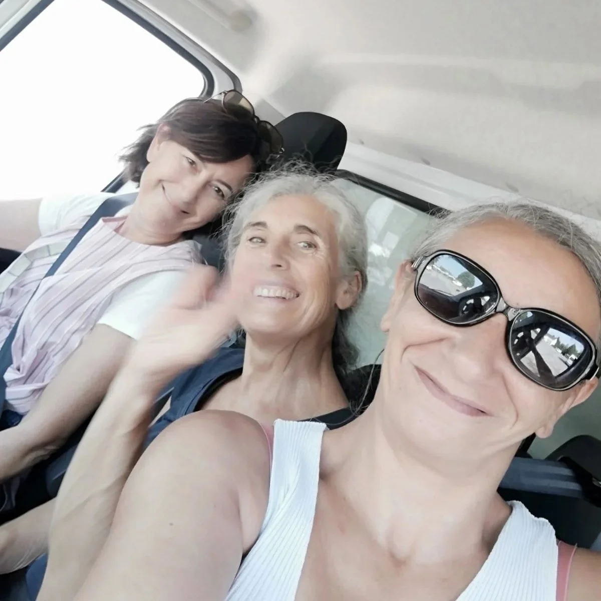 Quatre personnes souriantes prenant un selfie dans un véhicule, deux femmes et deux hommes, dont un porte des lunettes de soleil.