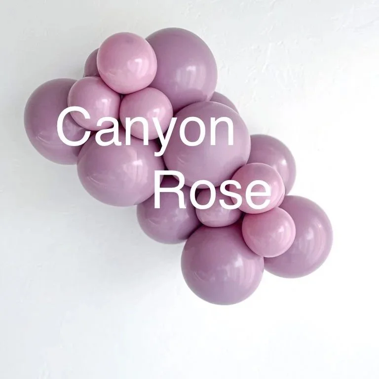 A cluster of pinkish-purple balloons arranged on a white surface with the words "Canyon Rose" written across the balloons.
