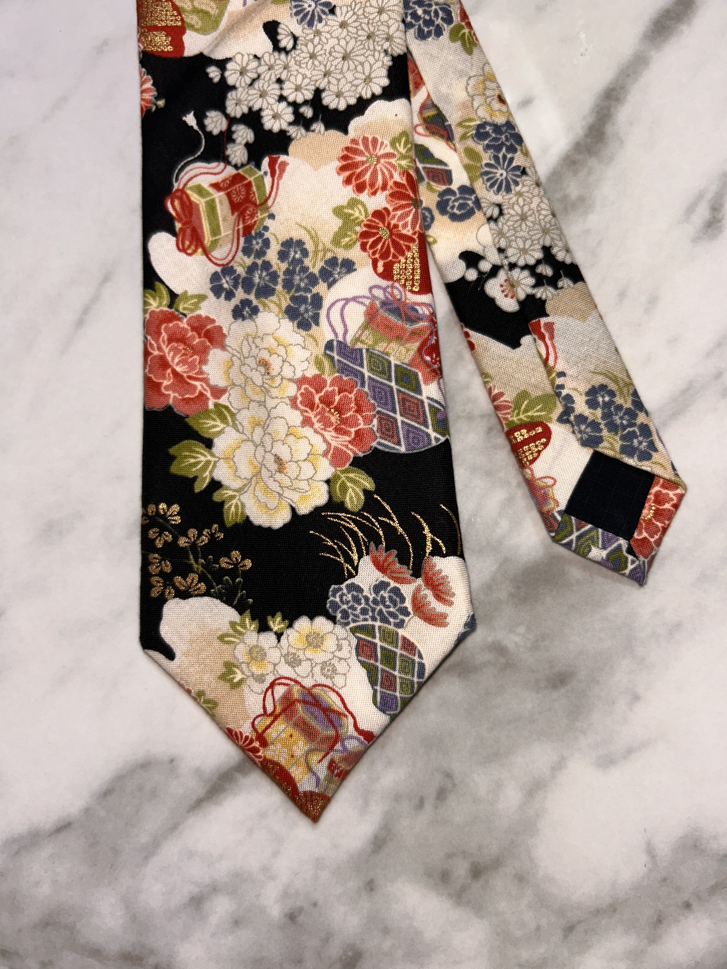 Close-up of a decorative fabric with traditional Japanese pattern, featuring flowers, geometric shapes, and vibrant colors, lying on a marble surface.