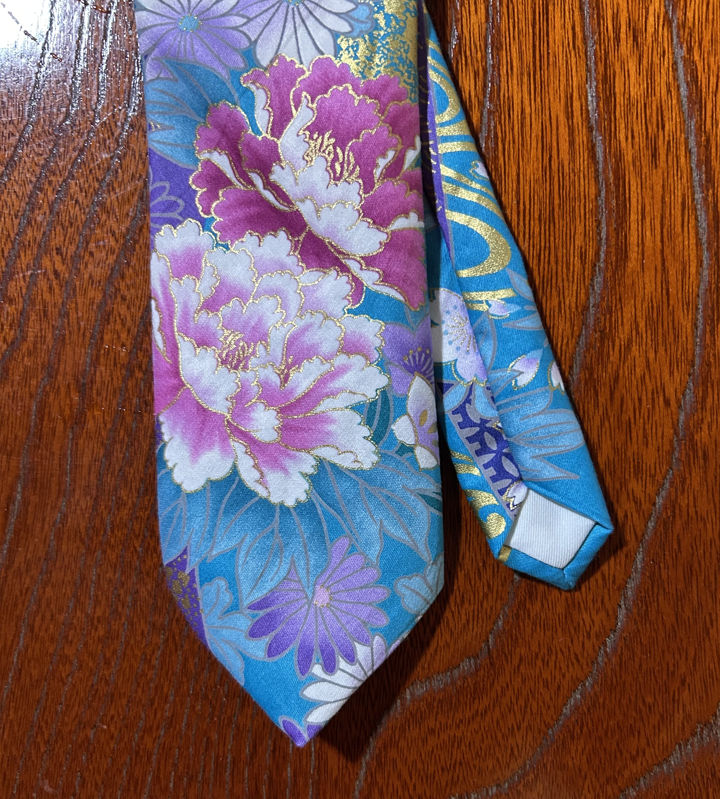 Close-up of a colorful fabric with floral and geometric patterns in pink, purple, blue, and gold, placed on a wooden surface.