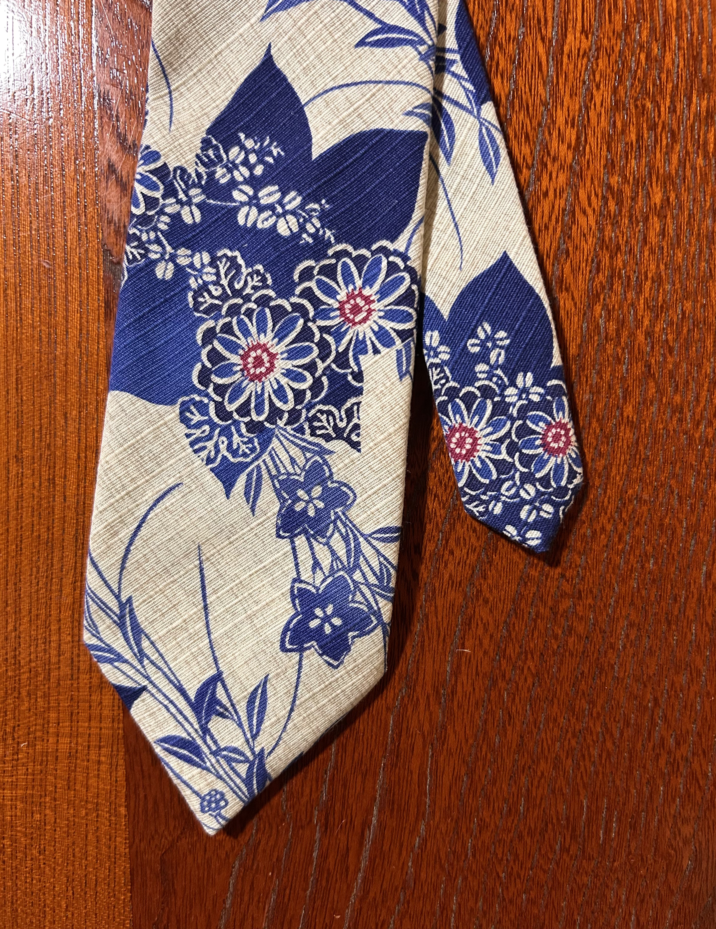 Close-up of a fabric with a cream background and blue floral and leaf pattern, placed on a reddish-brown wooden surface.