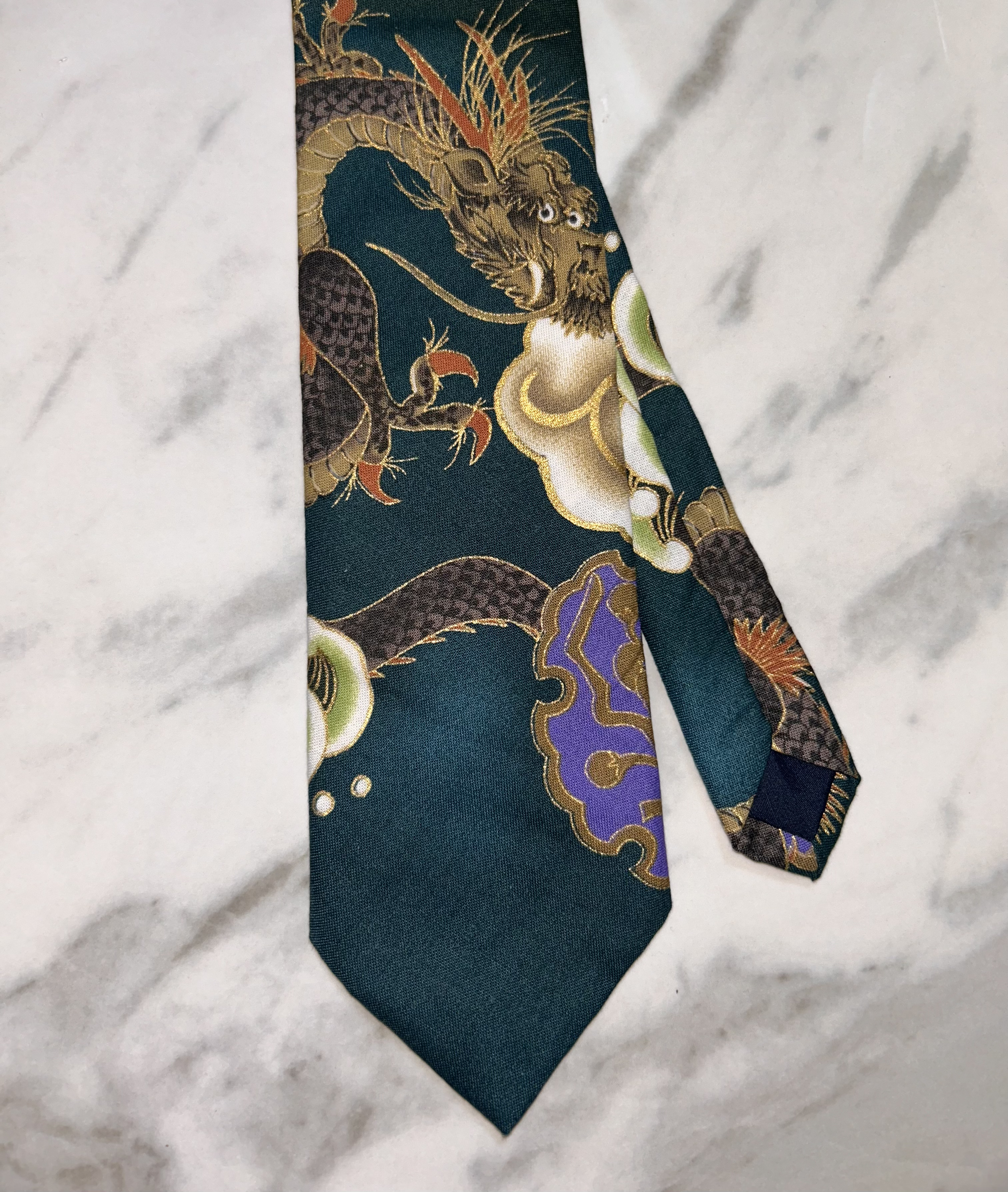 Close-up of a silk tied scarf with a dragon design on a white marble surface.