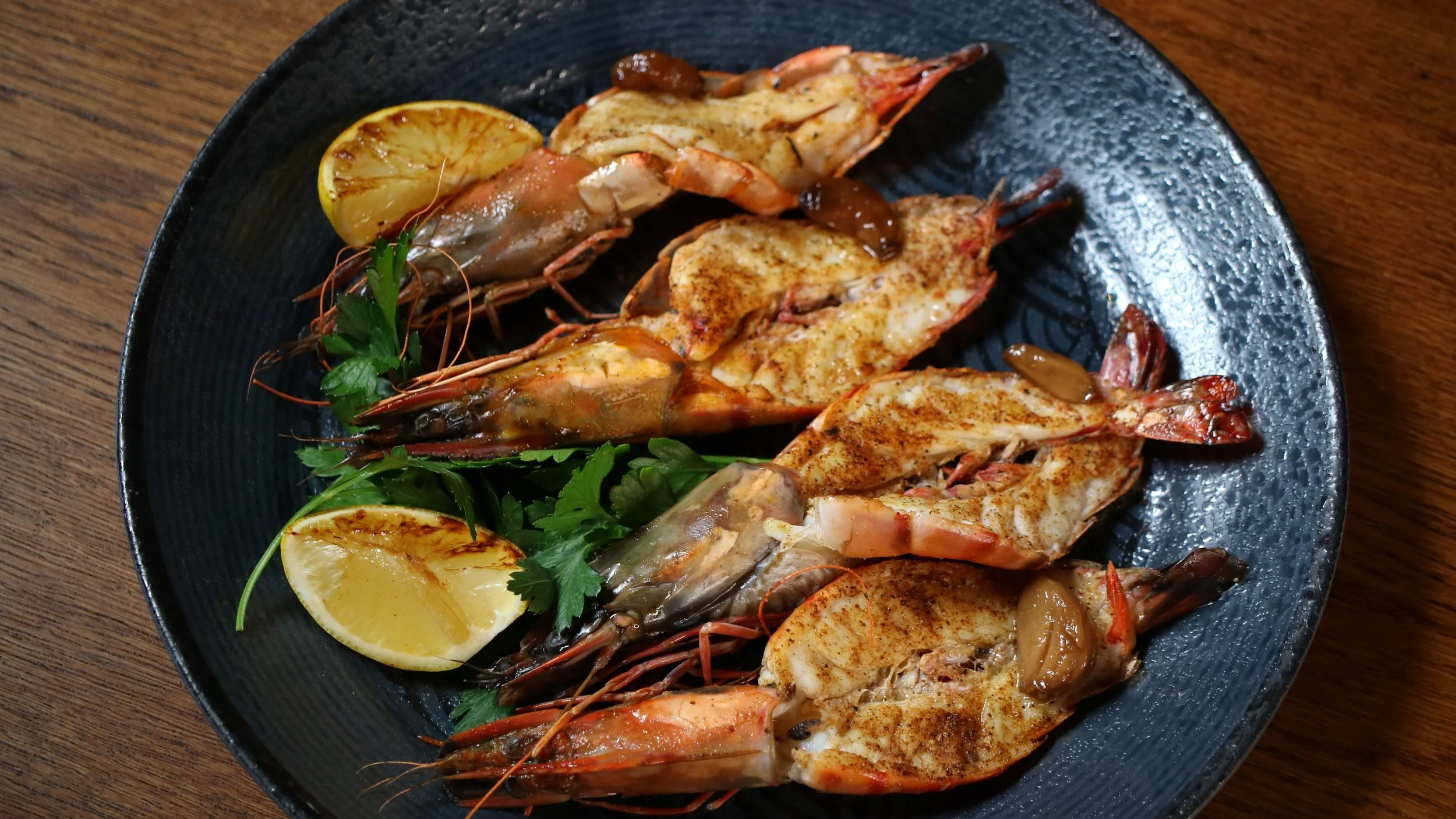 Grilled shrimp platter with lemon wedges and fresh herbs on a black plate