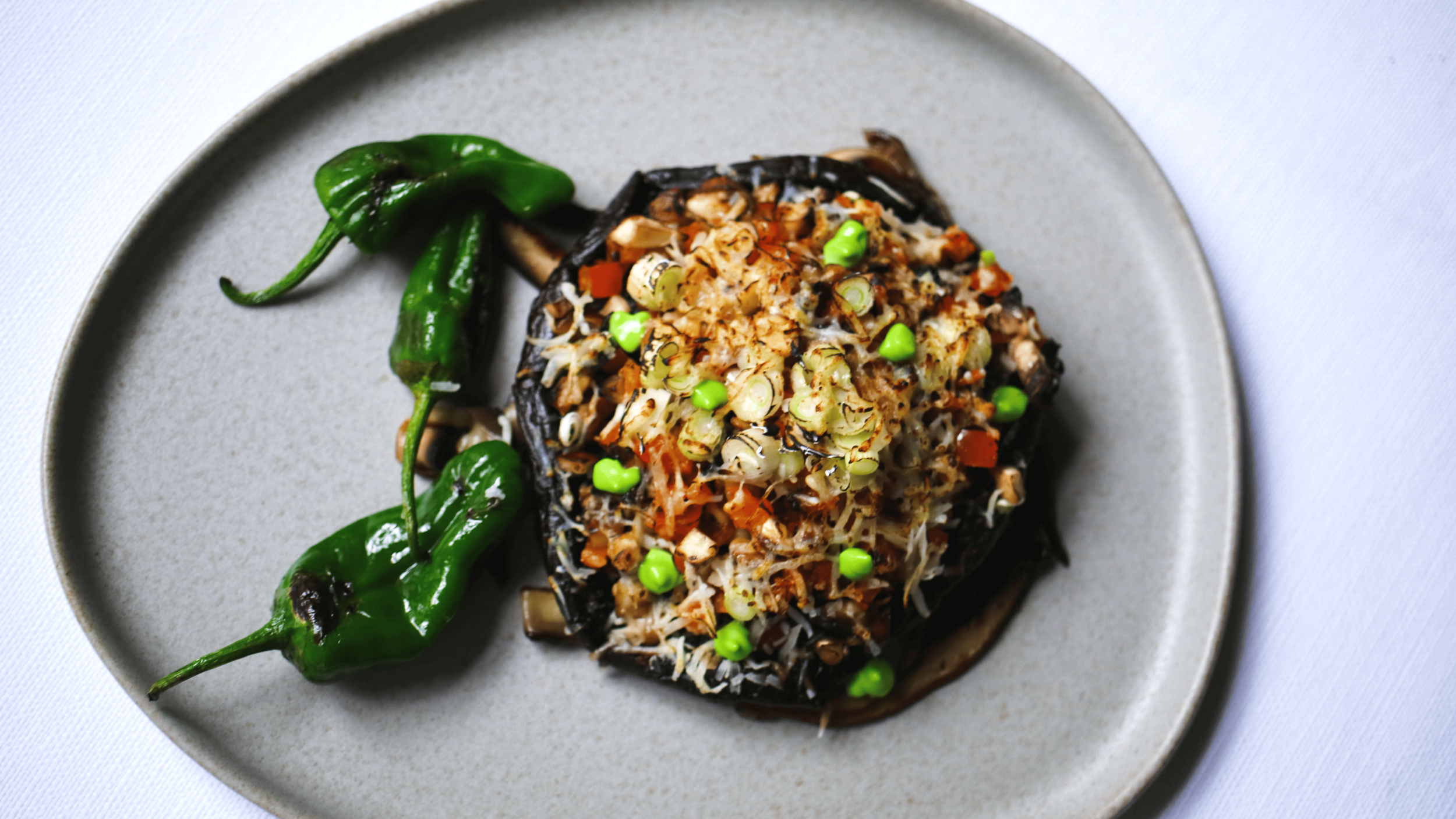 Baked eggplant topped with chopped vegetables and garnished with green peas, served on a ceramic plate.