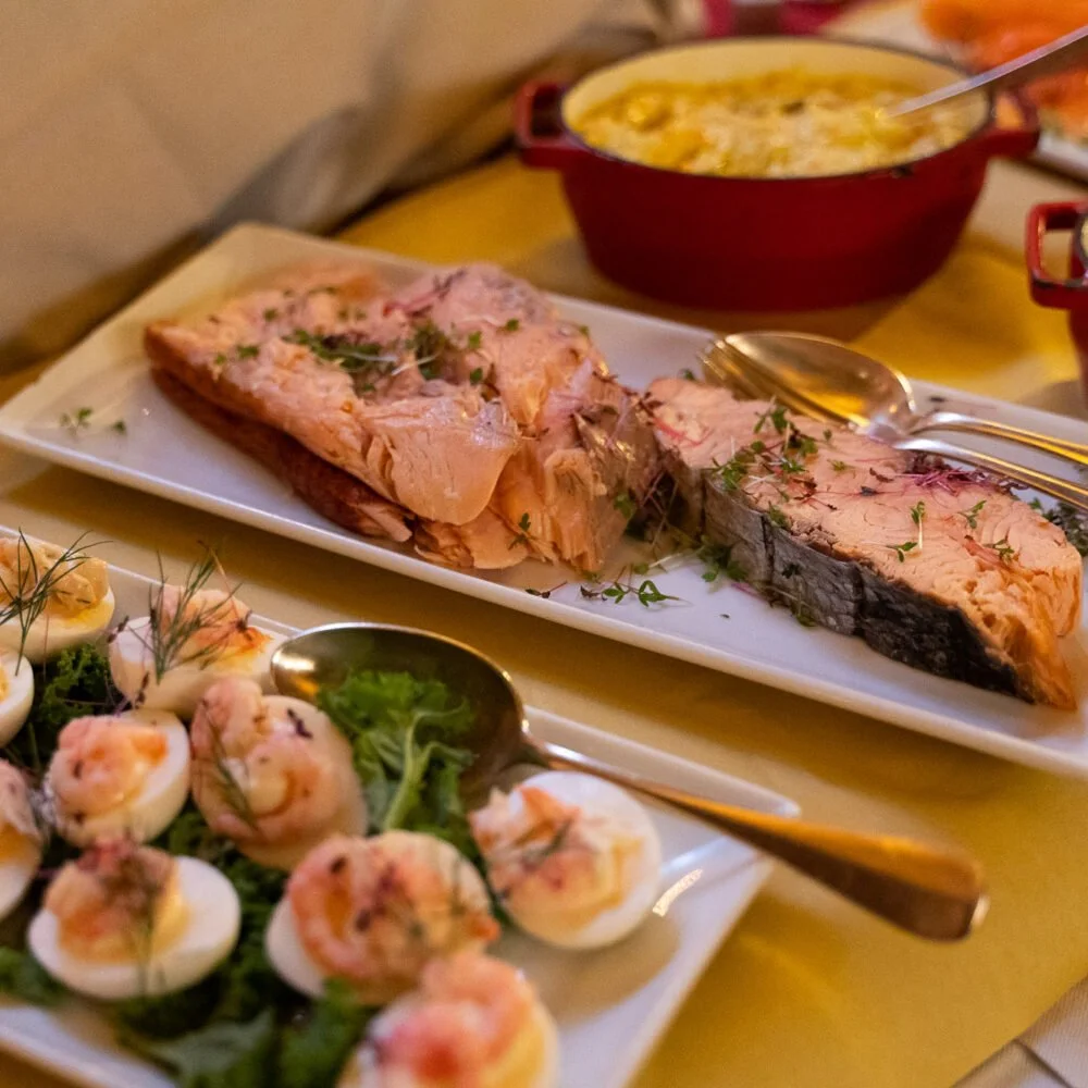 A plate with sliced cooked meat garnished with herbs, a bowl of creamy soup or casserole, and a platter of deviled eggs topped with shrimp and herbs.