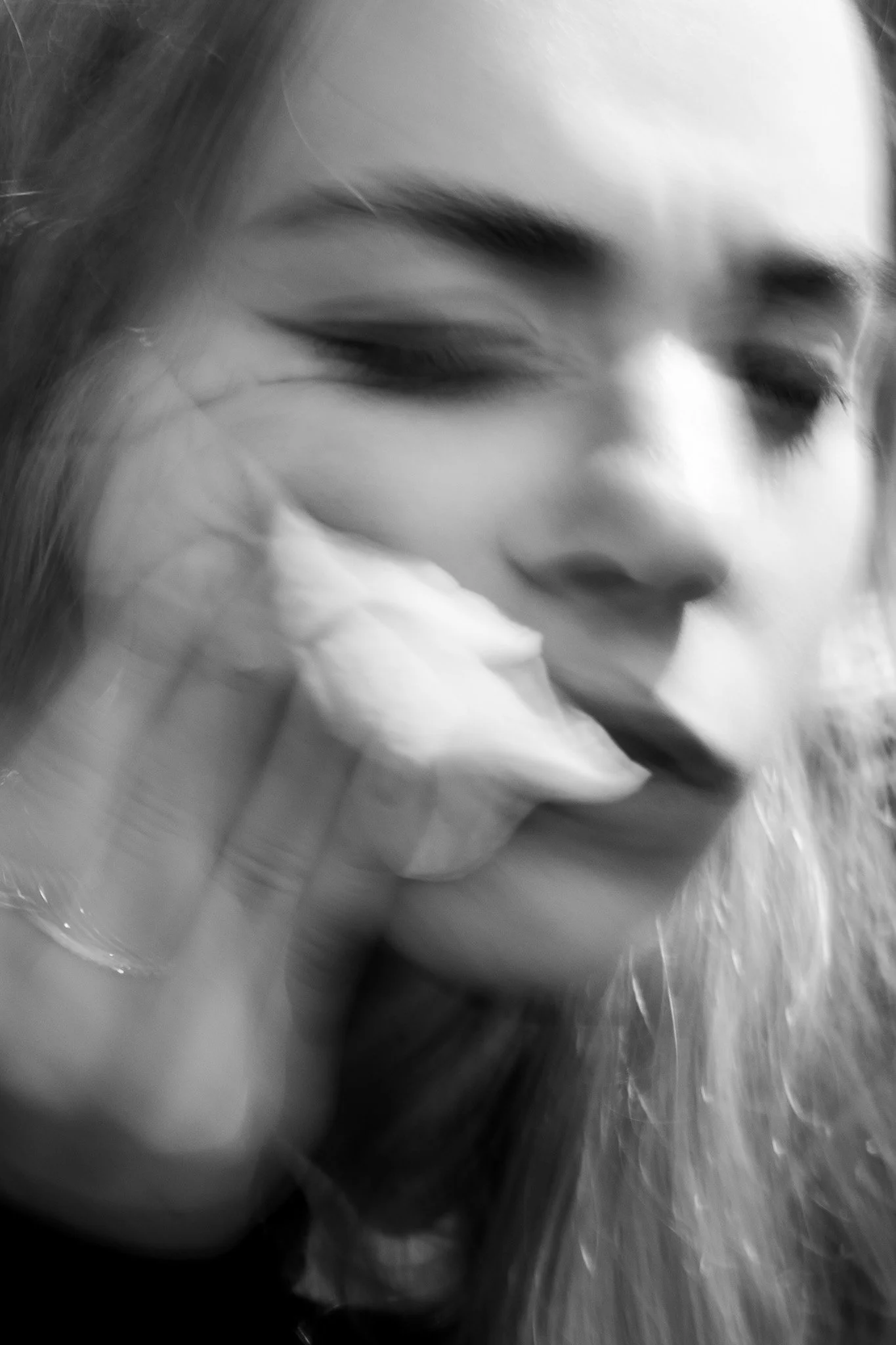 Close-up black and white photograph of a young woman's face, showing her eyes closed and a hand touching her cheek, with soft light highlighting her facial features.