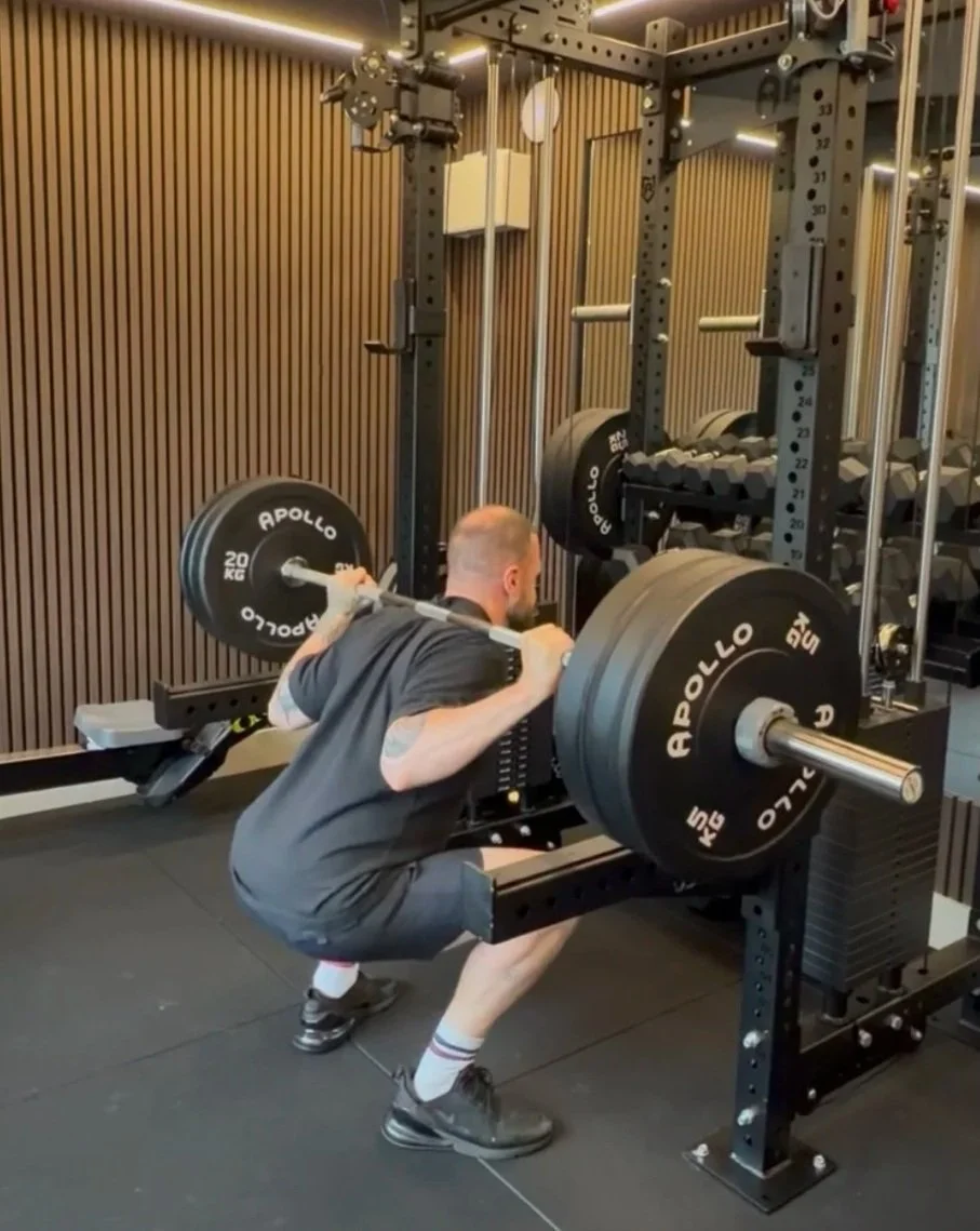 A man doing a barbell squat in a gym, with weights labeled Apollo.
