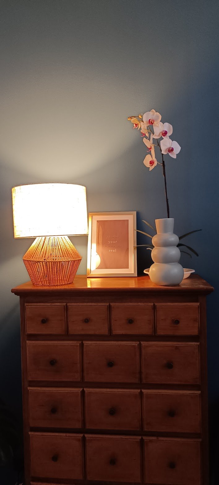 Comodino di legno con lampada, cornice con scritta, e vaso con orchidea