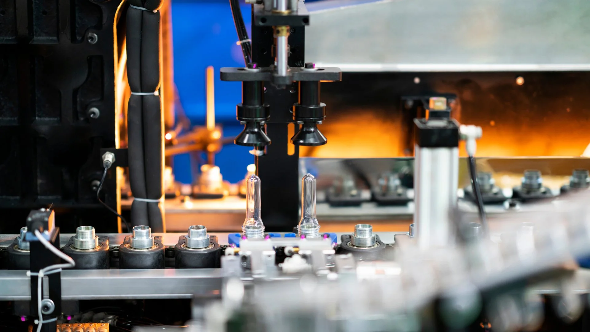 Close-up of a moulding machine forming clear plastic bottle preforms on a factory production line.