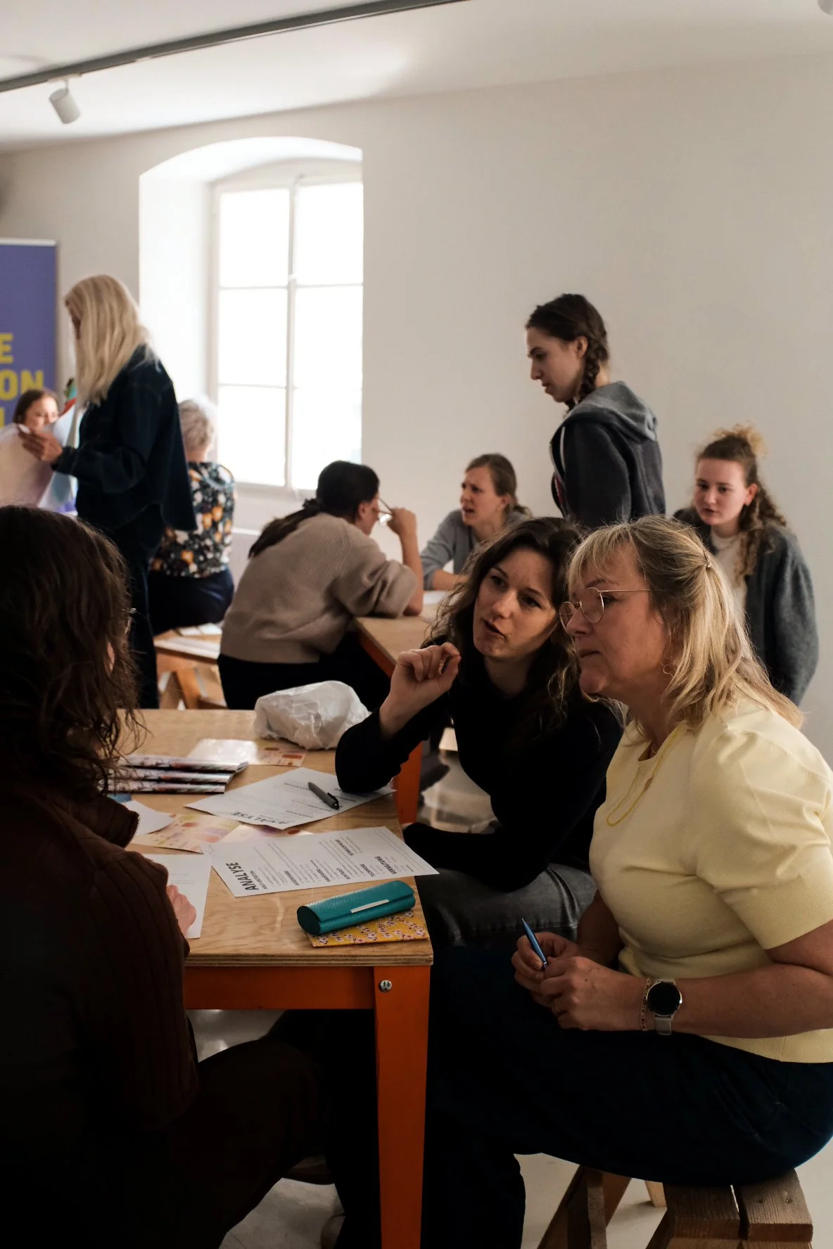 Mehrere Menschen sitzen an einem Tisch und unterhalten sich in einem hellen Raum mit großen Fenstern bei einem Farbanalyse-Workshop von Studio Barb.