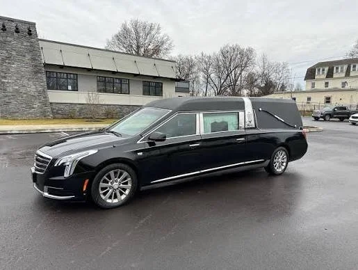 Black hearse parked on wet pavement in a residential area.
