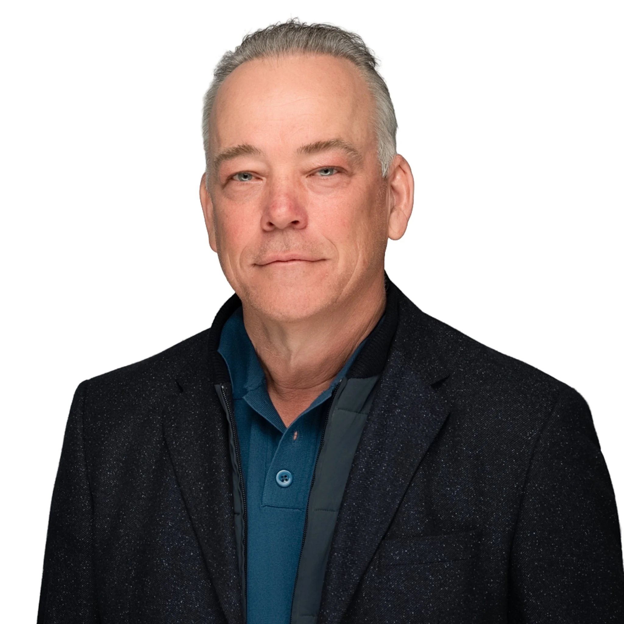 Close-up of a middle-aged man with short gray hair, blue eyes, and a light complexion, dressed in a dark speckled blazer over a teal shirt with a dark vest, against a plain white background.