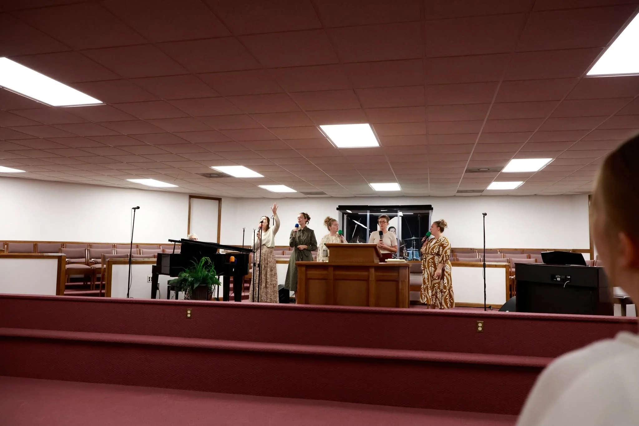Church service with women speakers at the pulpit, raising hands, and gathered congregation.