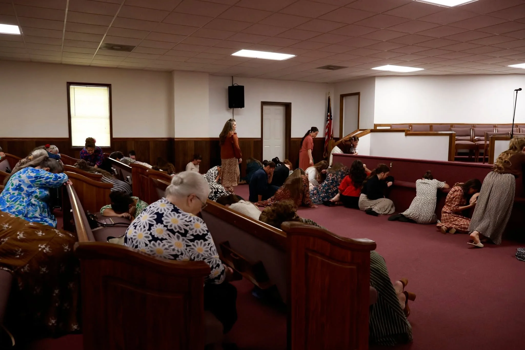 People kneeling and praying inside a church or assembly hall.