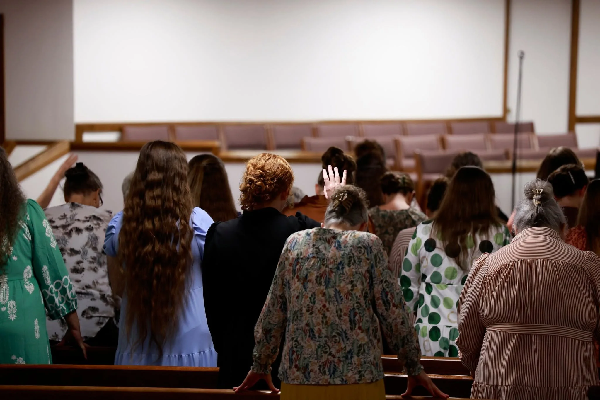 People sitting in a church or auditorium listening to a speaker, with some raising their hands.