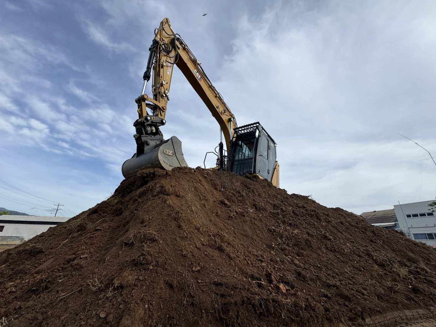 A bulldozer on a dirt mound, with a cloudy sky and some buildings in the background.