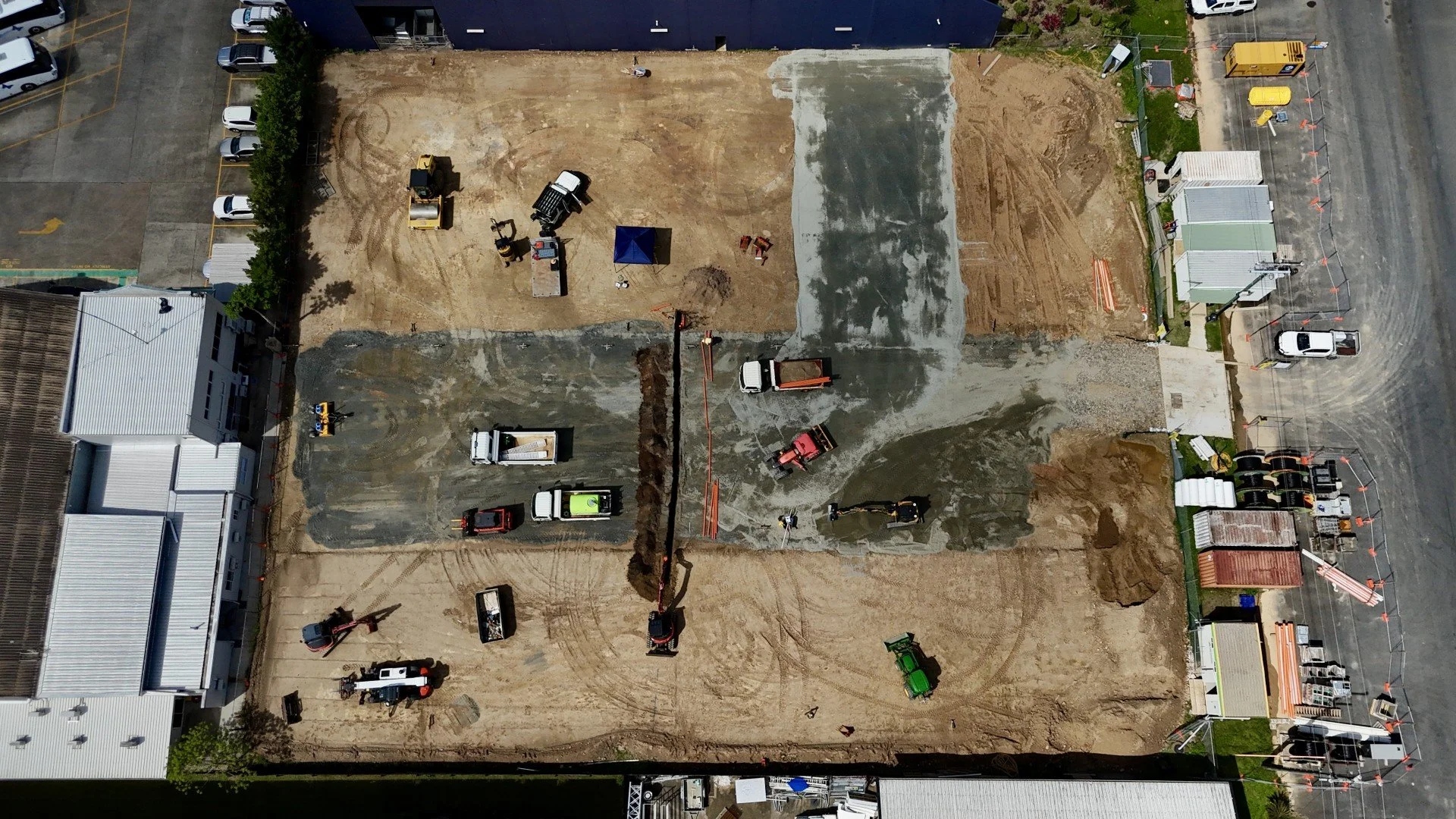 An aerial view of a construction site with various heavy machinery and vehicles, surrounded by parking lot and buildings.