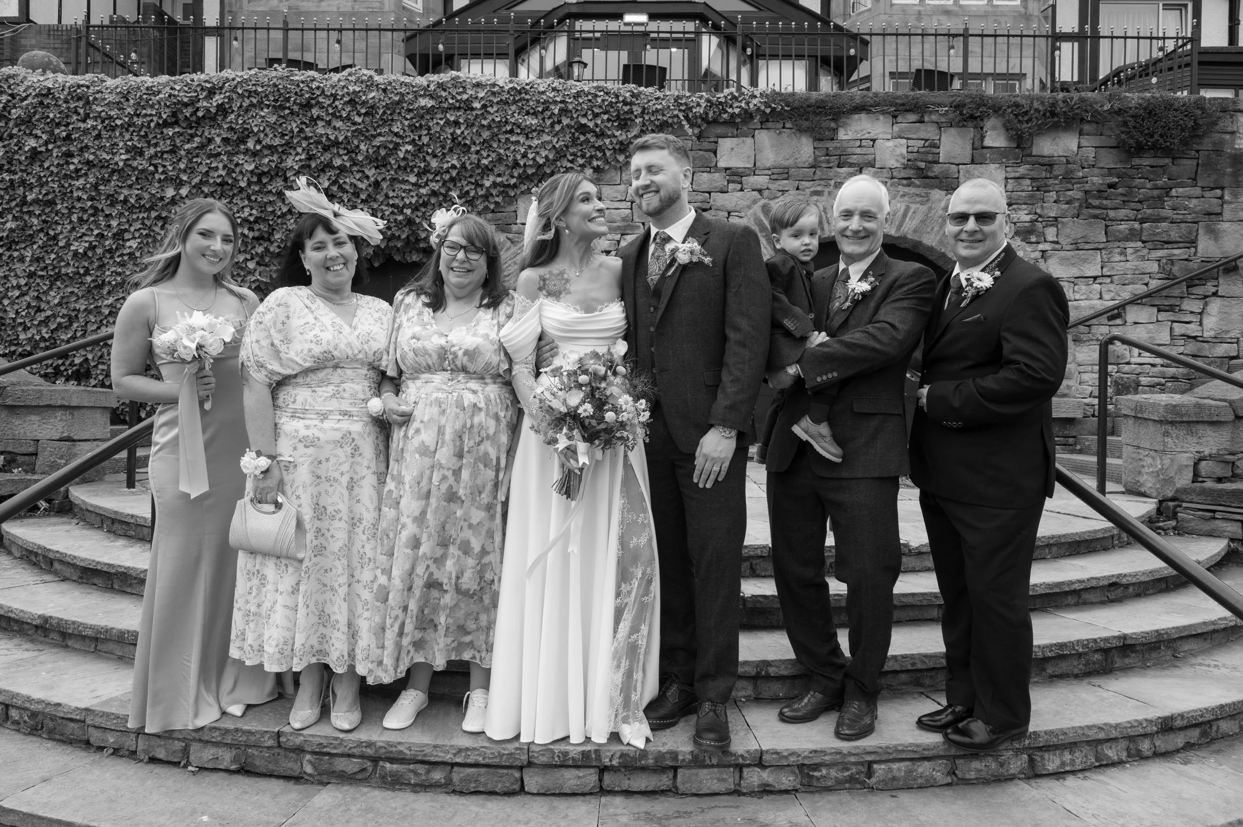 Black and white photo of a bride and groom with family members and friends standing on steps outside, celebrating at a wedding.