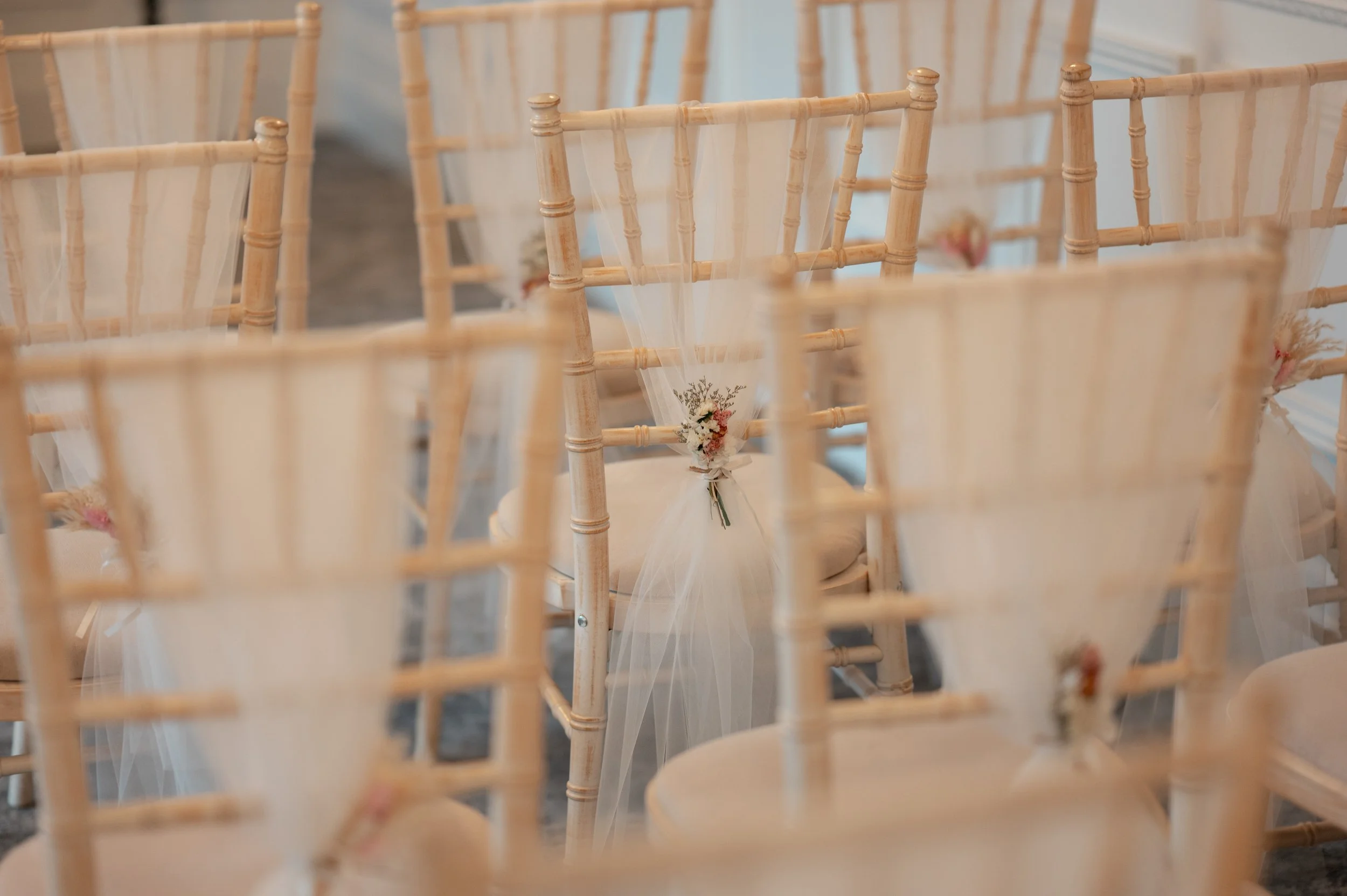 Empty wooden chairs decorated with small flower arrangements for an event or wedding.