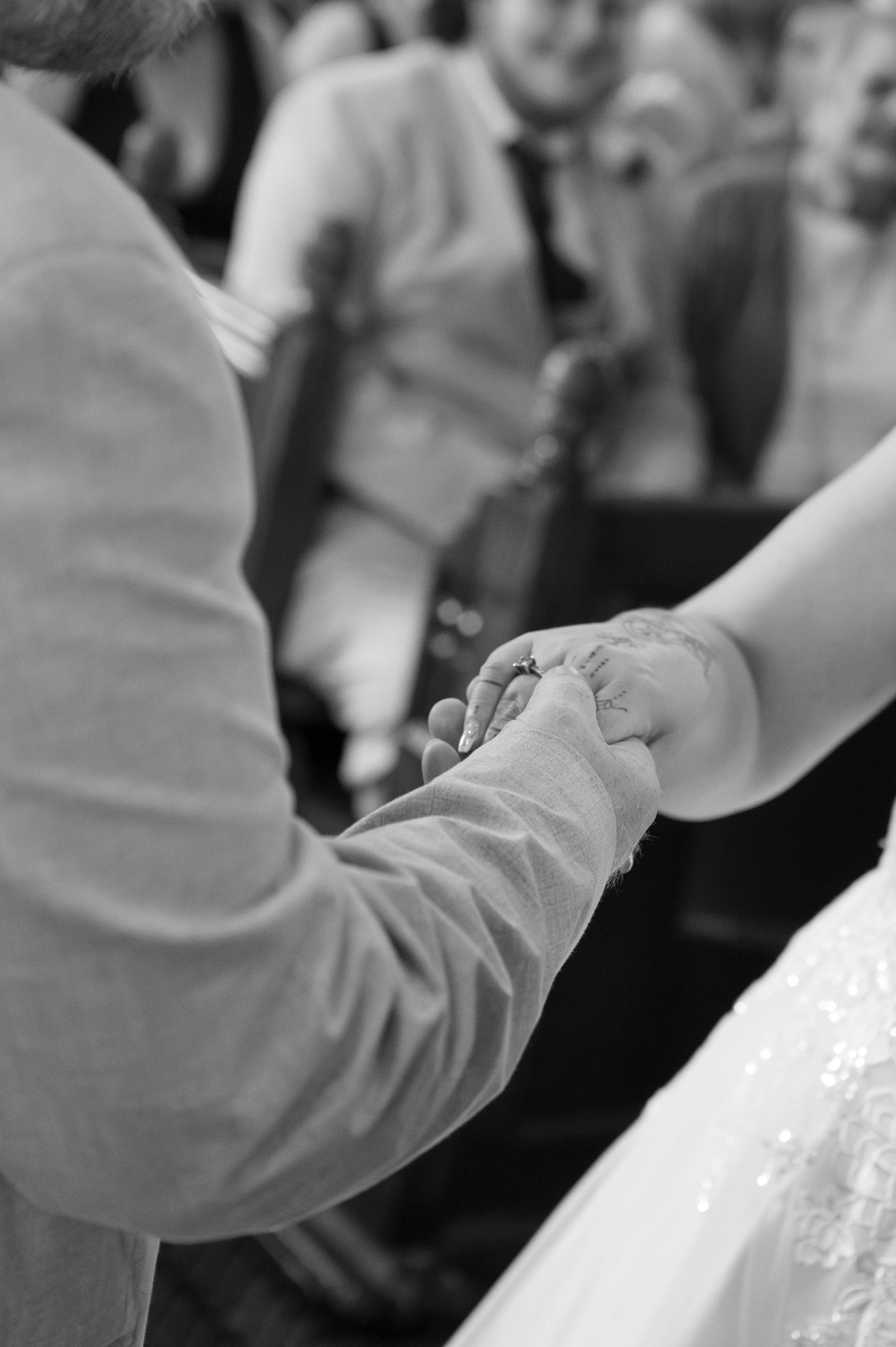 People holding hands during a ceremony, possibly a wedding, with a table decorated with flowers in the foreground.
