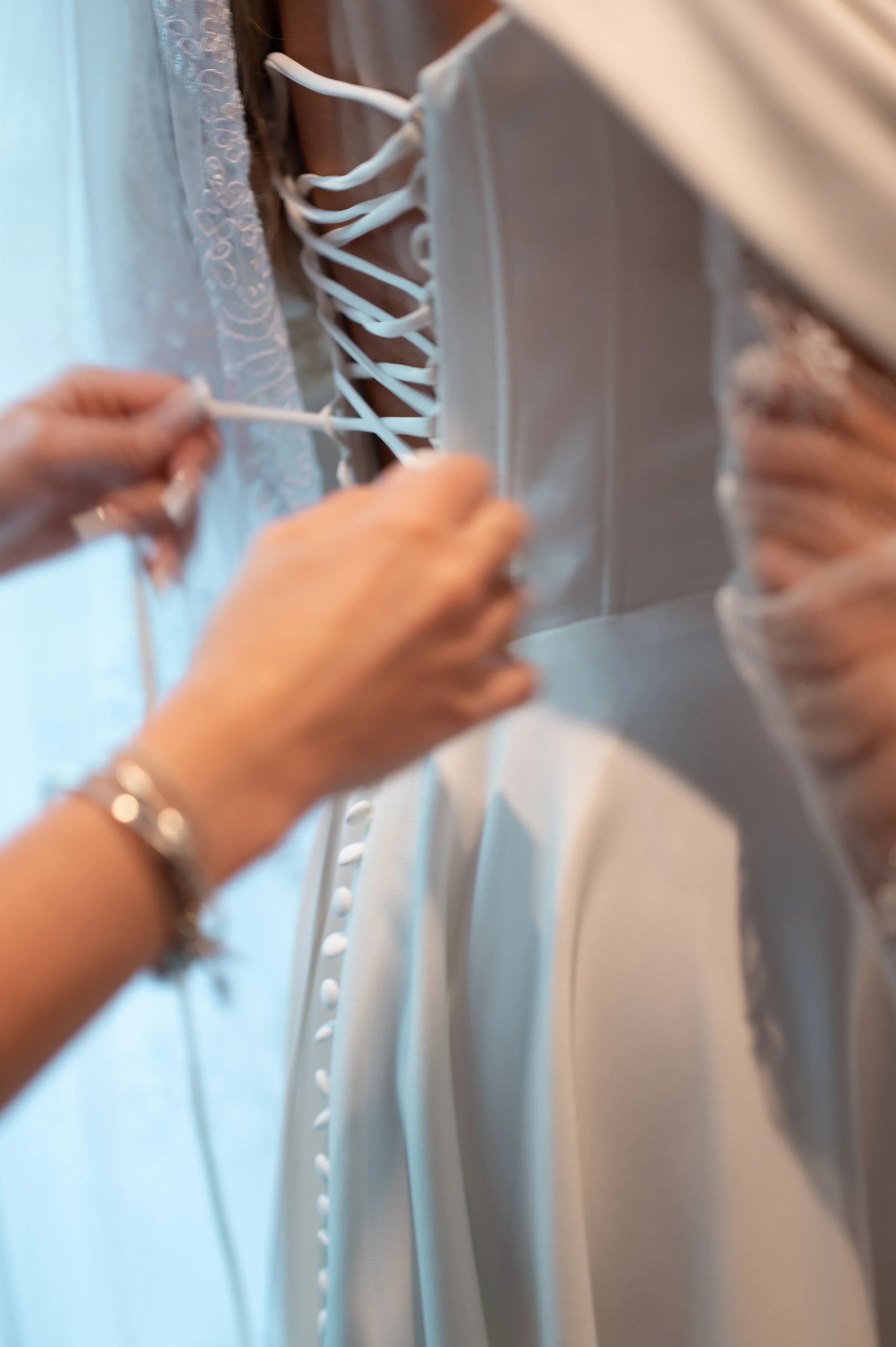 Close-up image of hands tying the laces of a white dress with button details.