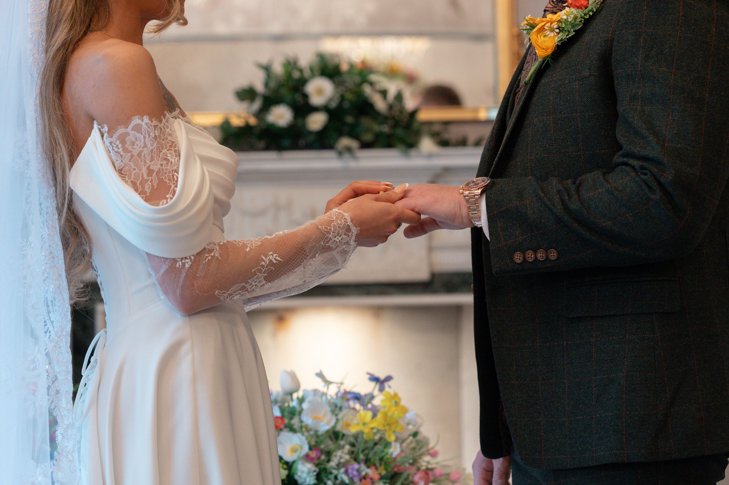 A bride and groom holding hands during their wedding ceremony in a church, with flowers in the background.